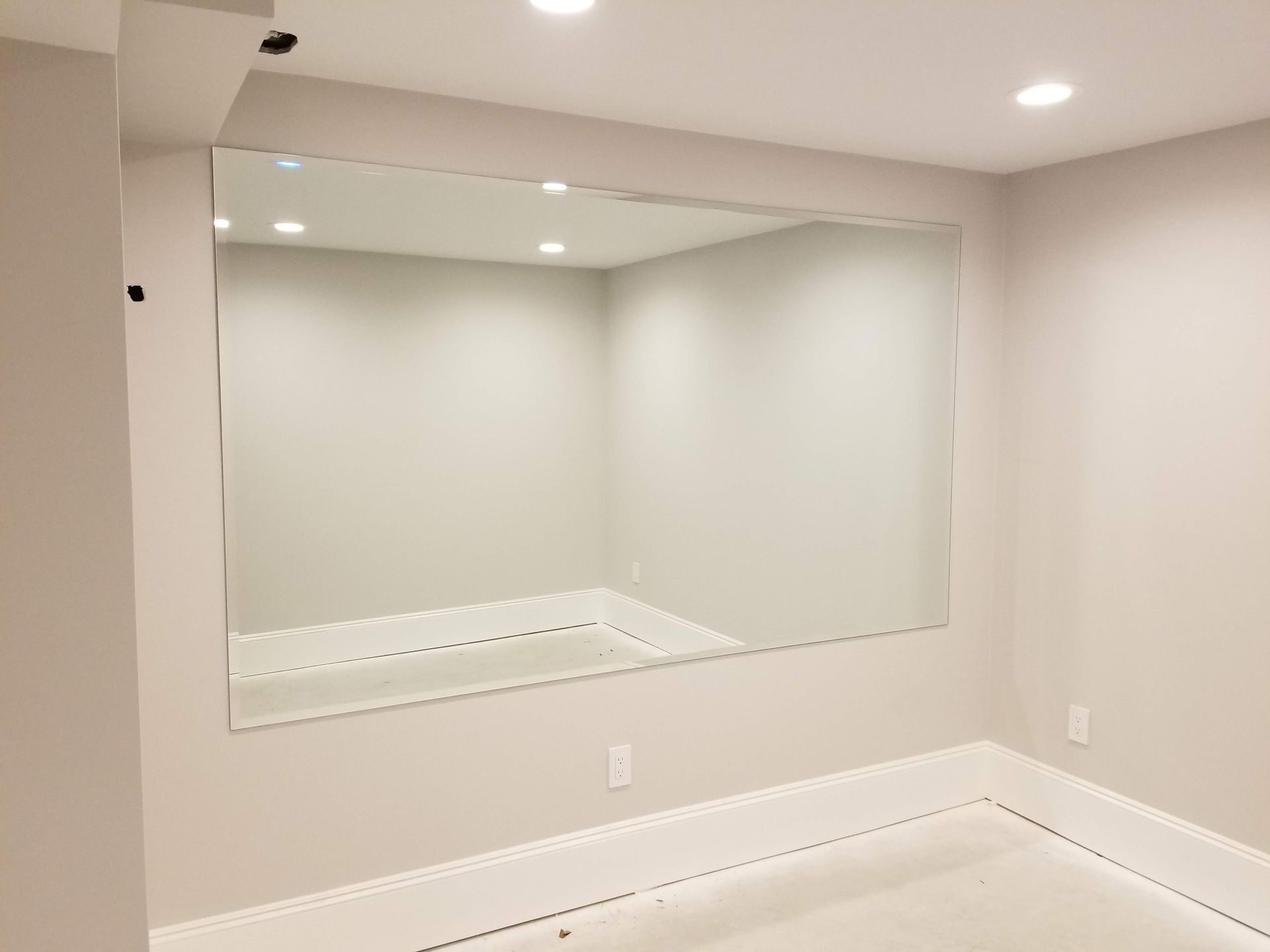 Large rectangular wall mirror in a room with white walls and recessed lighting.