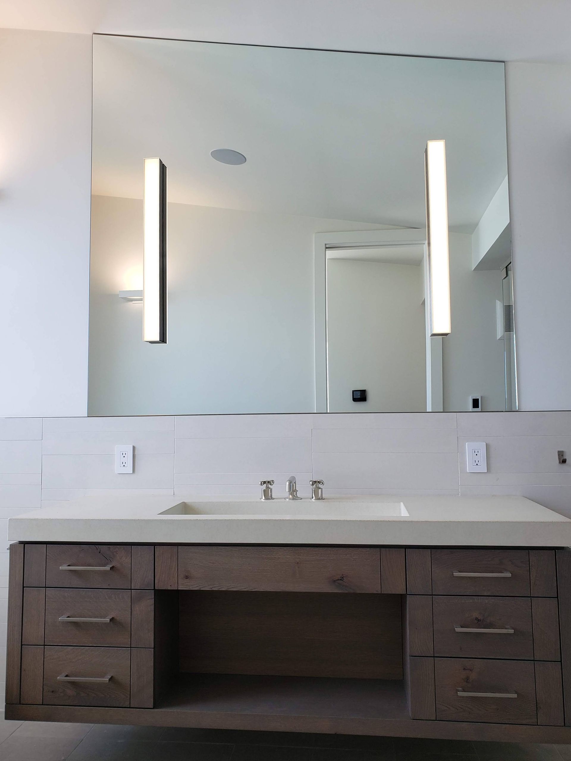 Bathroom vanity with large mirror and vertical lights. White walls, wood cabinet, and sink.