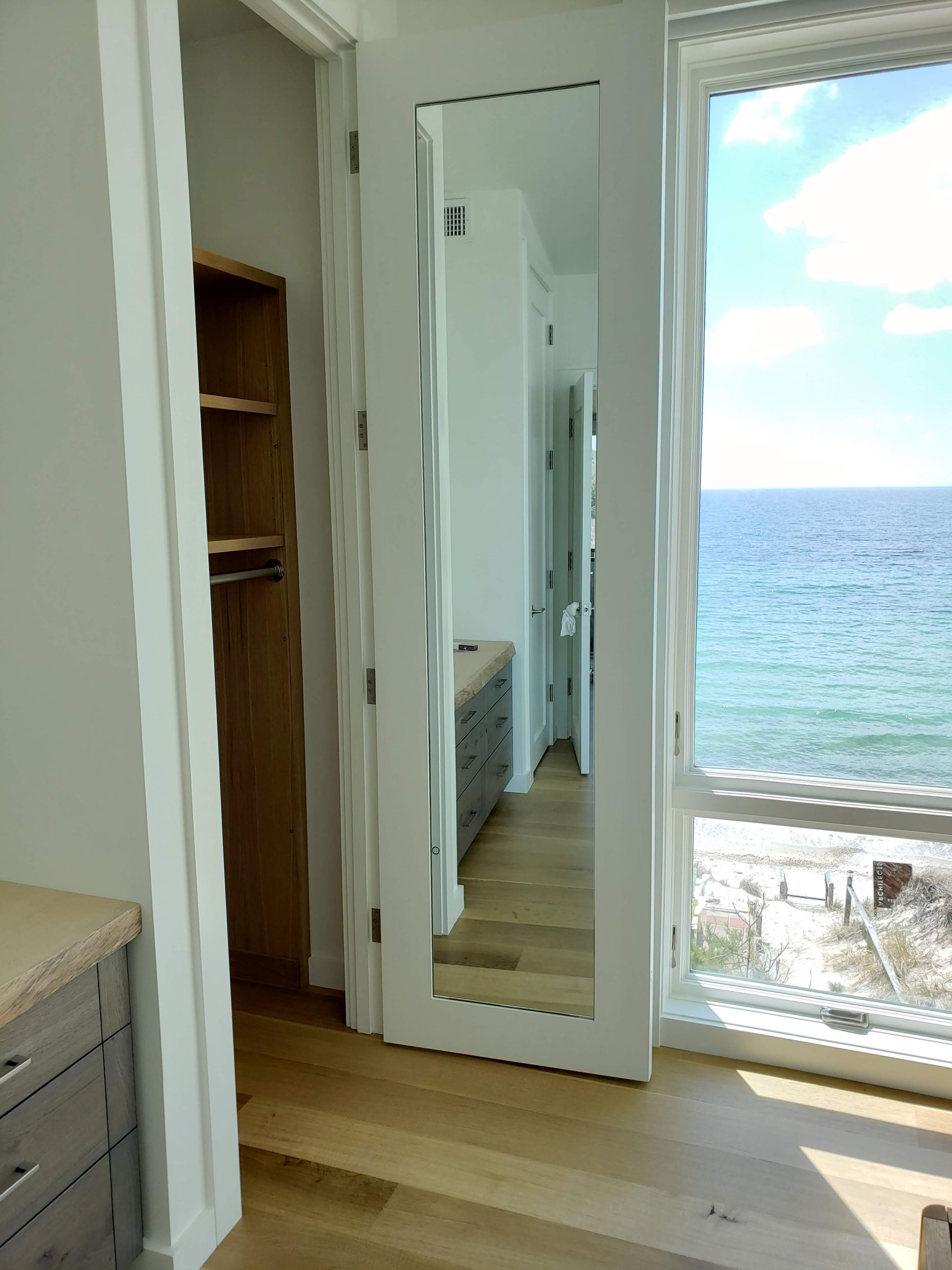 A walk-in closet with a full-length mirror, wooden shelves, and an ocean view through a window.