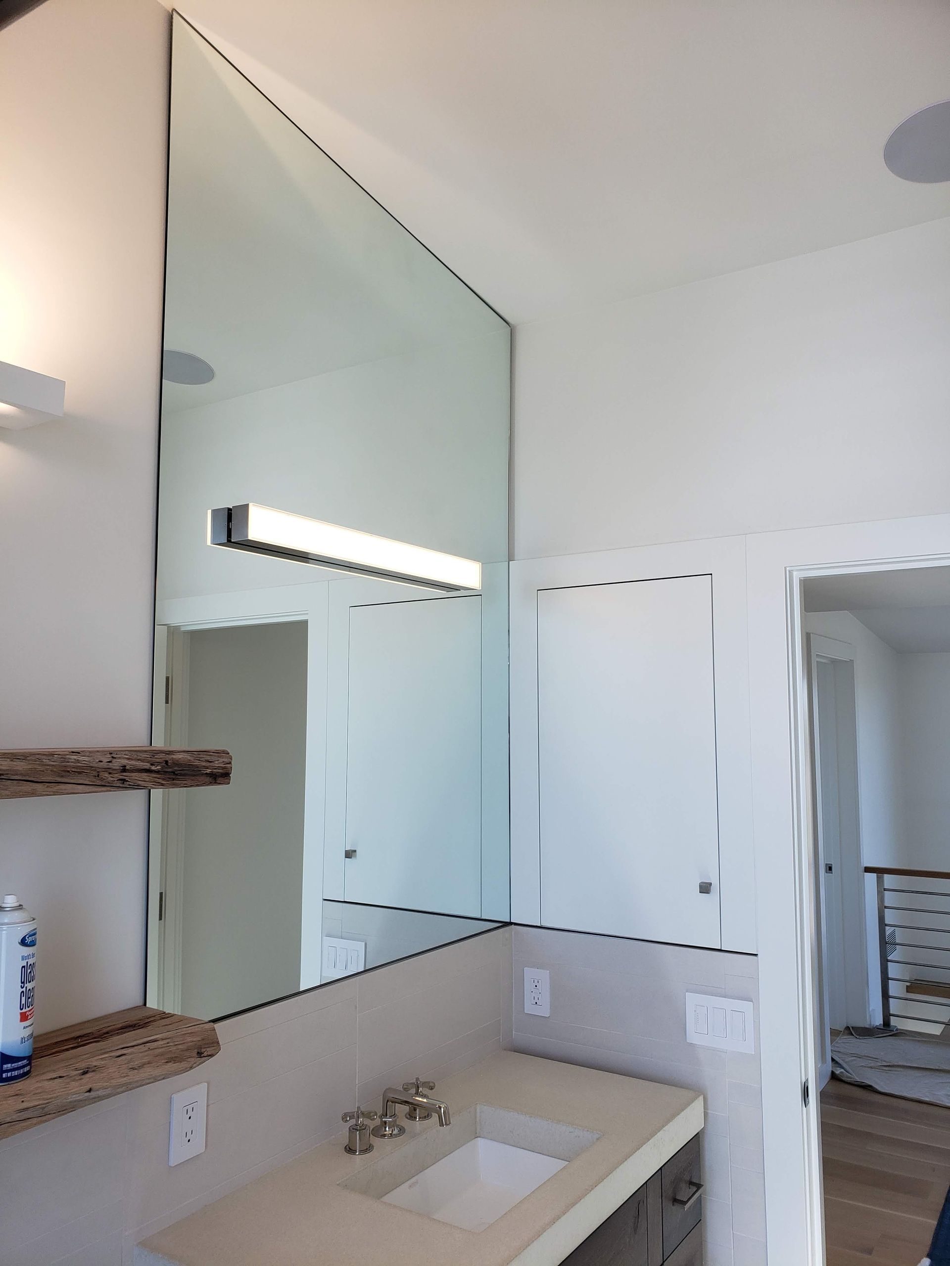 Bathroom with large angled mirror, countertop sink, and overhead light. White walls and door frame.