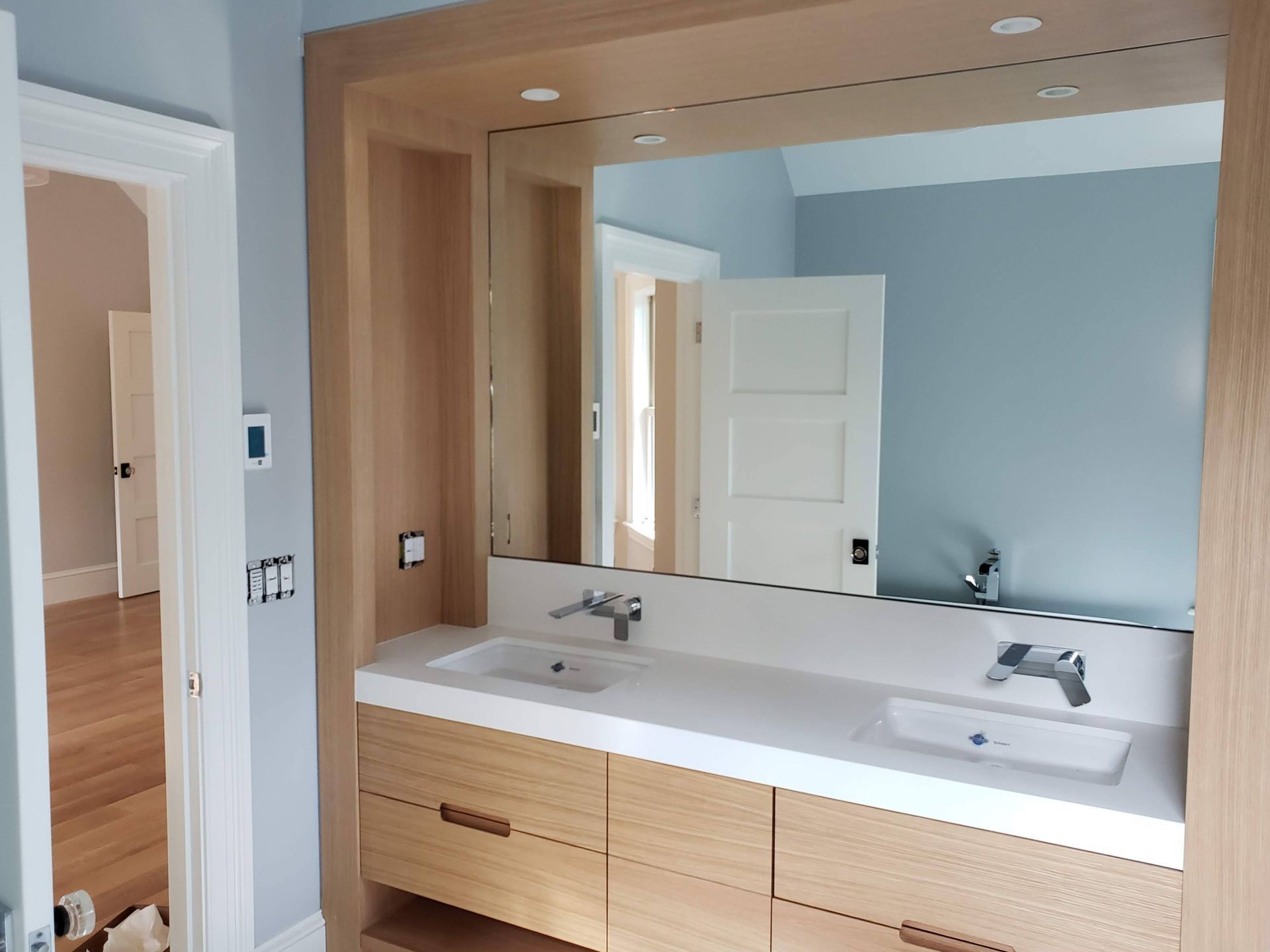 Bathroom vanity with double sinks, large mirror, light wood cabinets, and light blue walls.