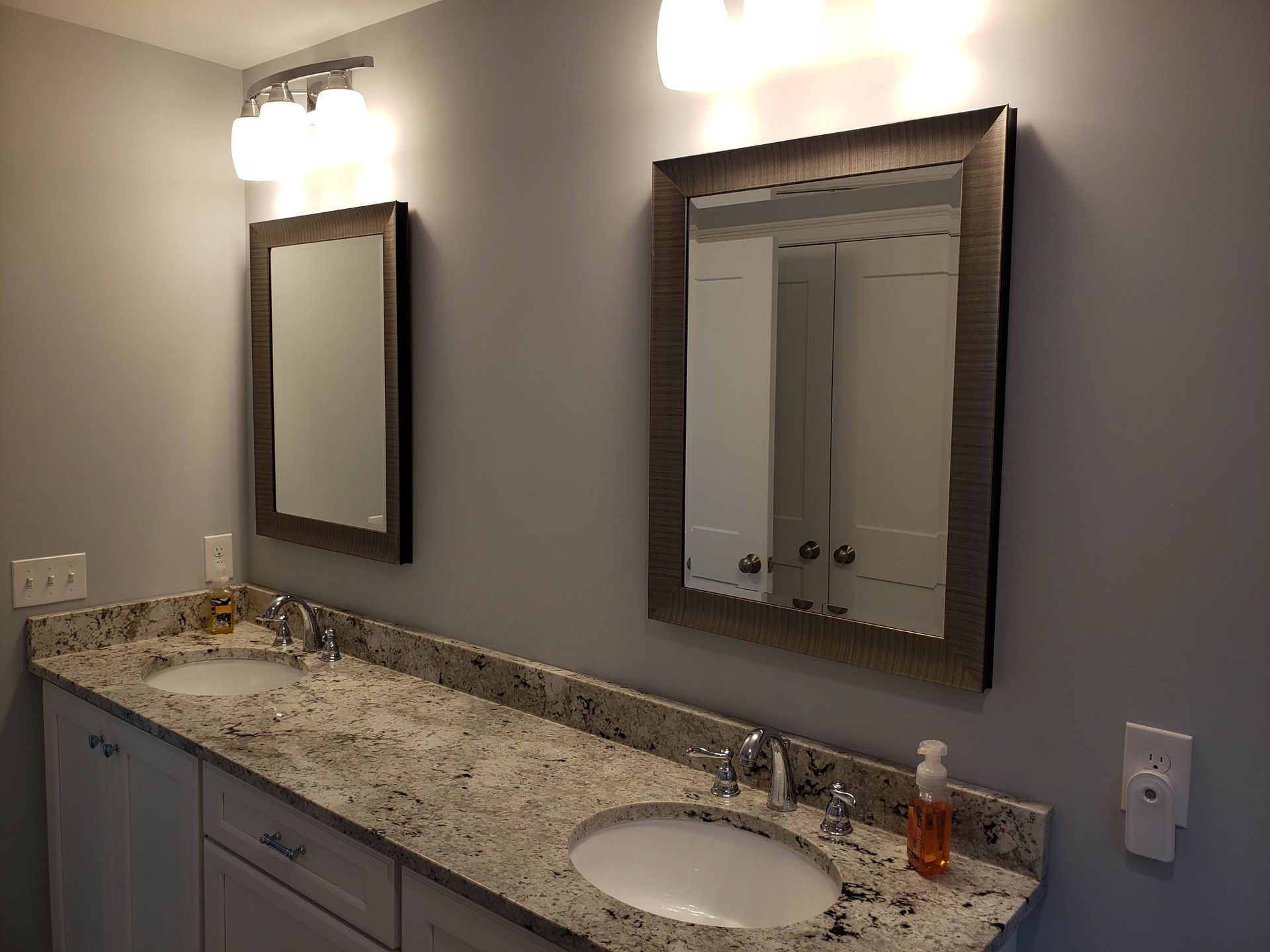 Bathroom with two sinks, mirrors, and lights, granite countertop, and gray walls.