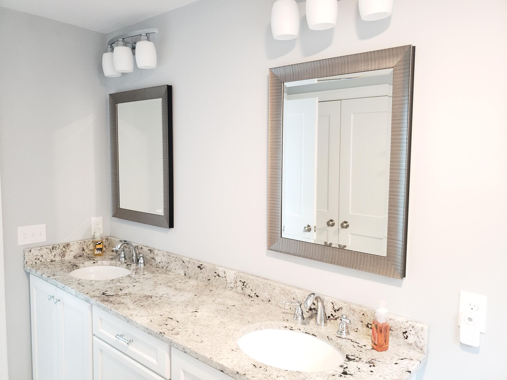 Bathroom with a double vanity. White cabinets, granite countertop, two sinks, mirrors, and silver lighting fixtures.