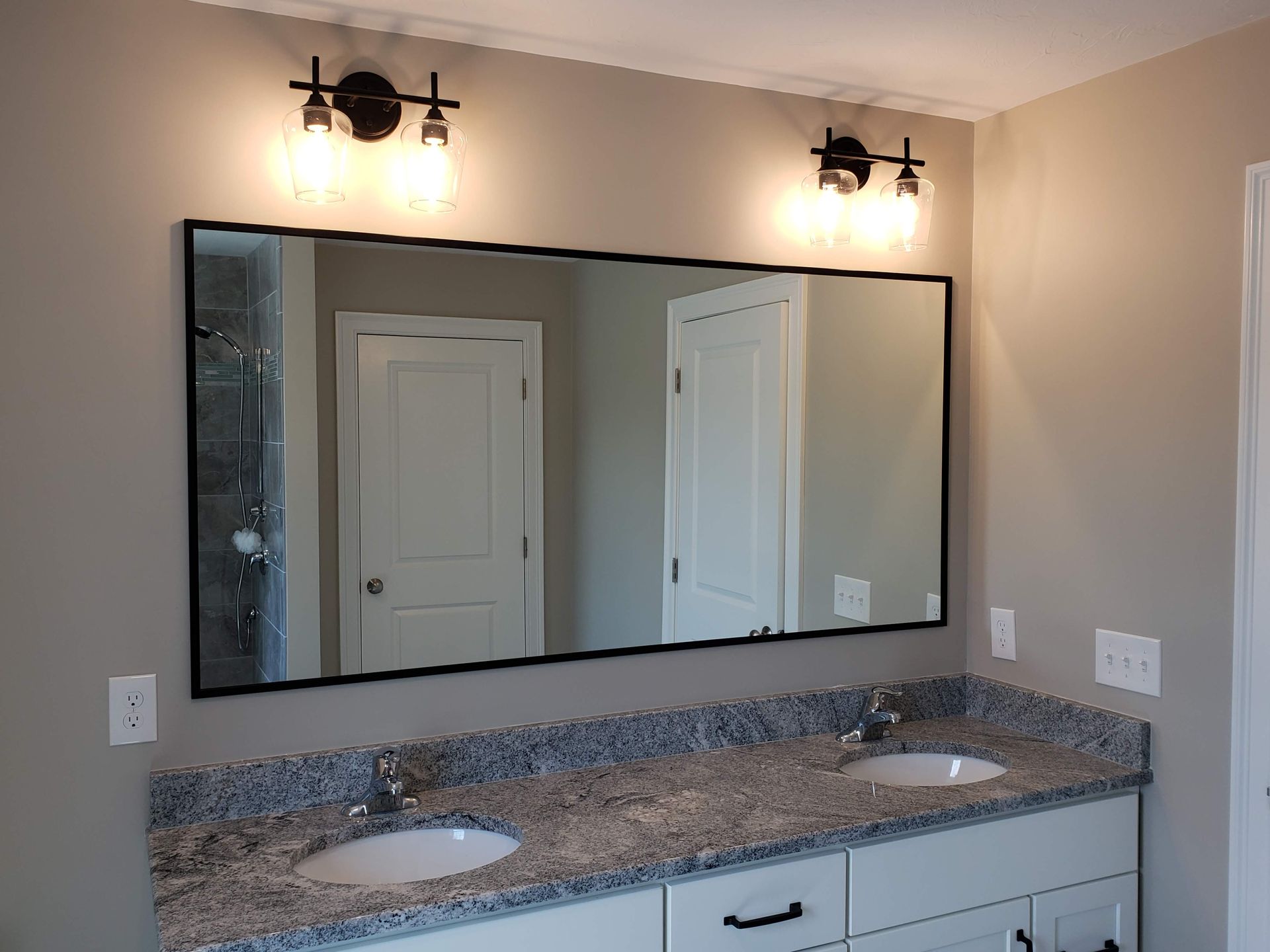 Bathroom with a rectangular mirror, two light fixtures, a double sink vanity, and granite countertop.