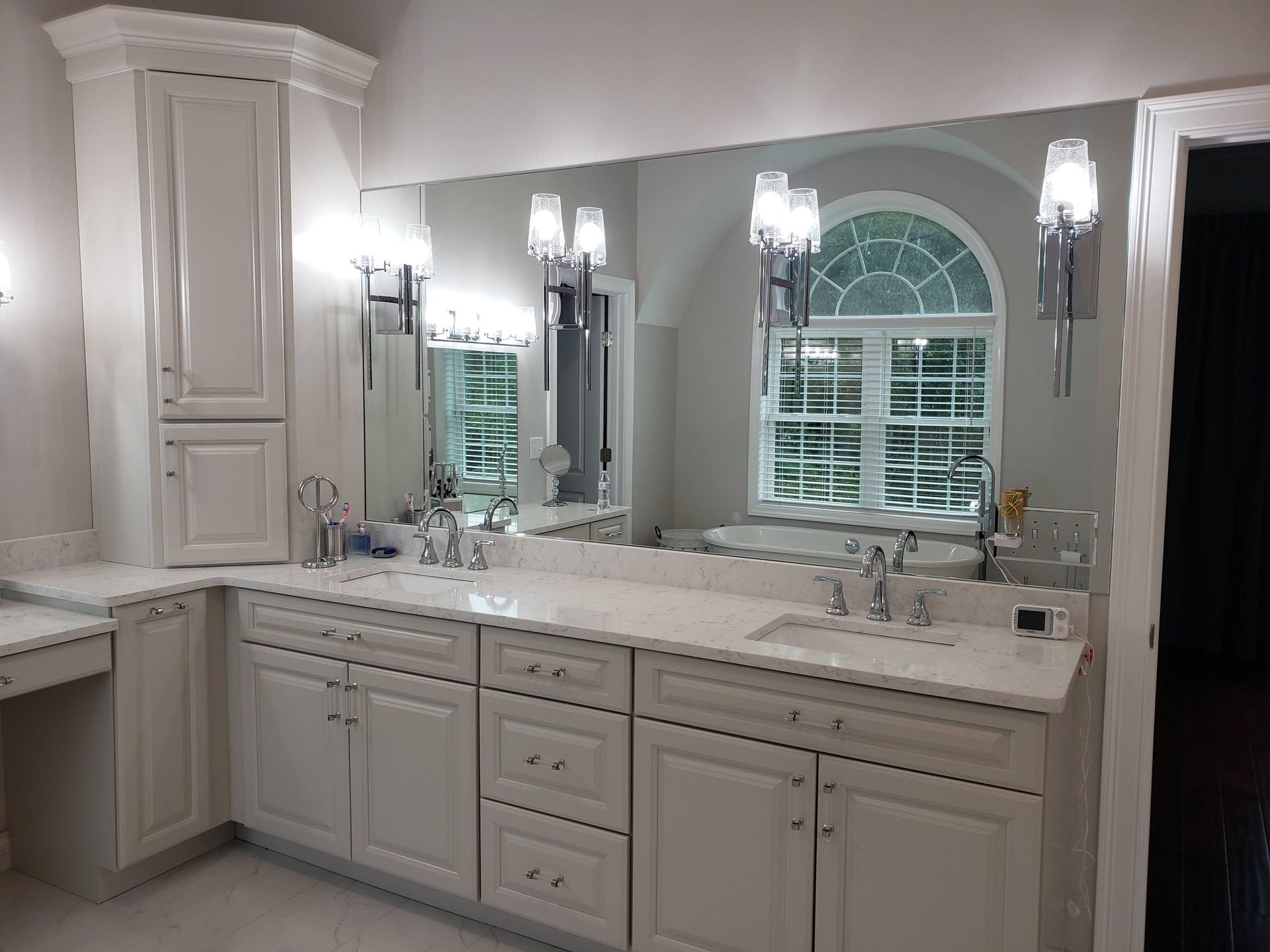 Bathroom with large mirror, white cabinets, marble countertop, and chrome fixtures.