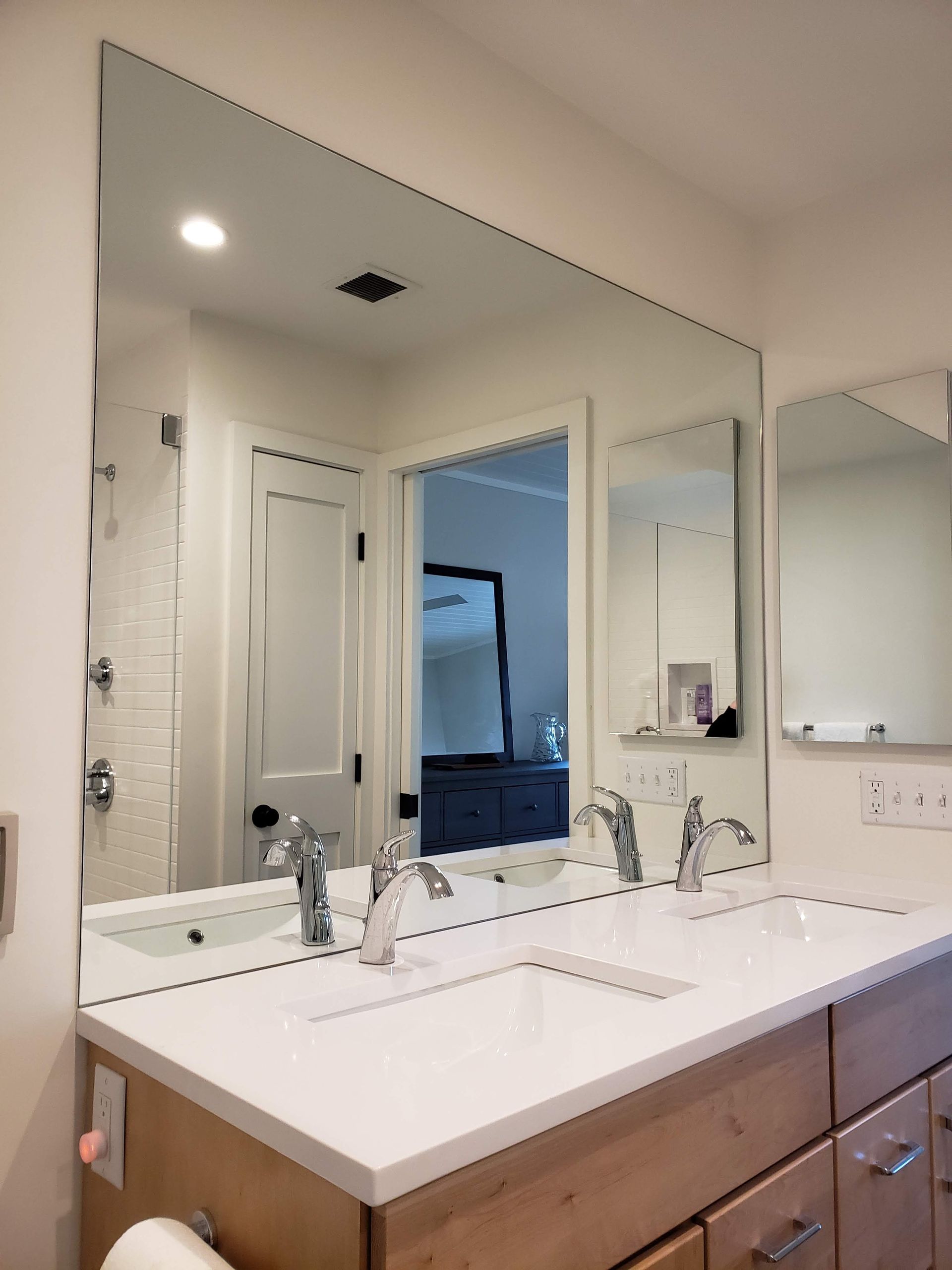 Bathroom with large rectangular mirror above double sinks on a wooden cabinet, with a view of another room.