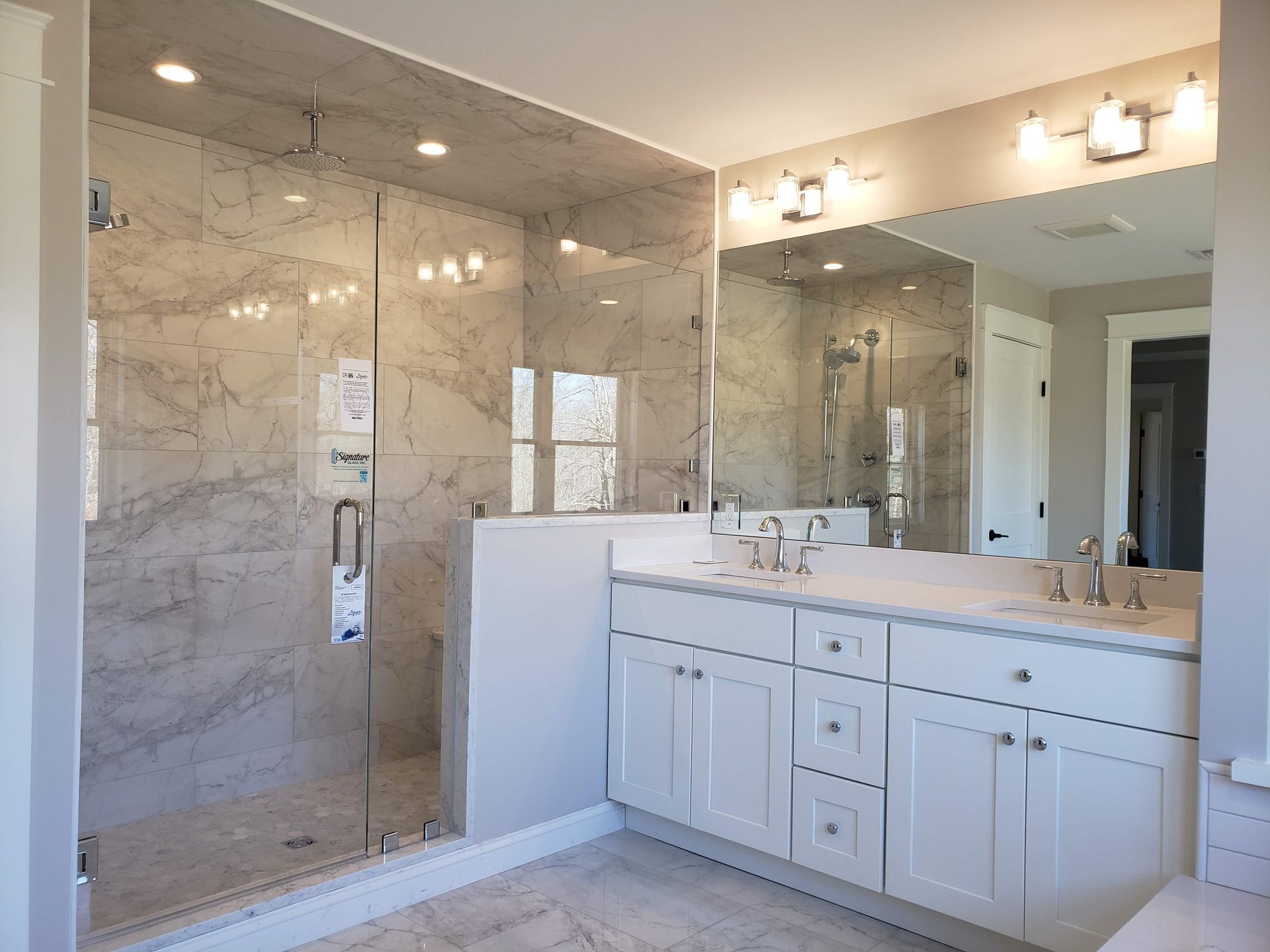 Bathroom with marble-like shower, white vanity, and large mirror.