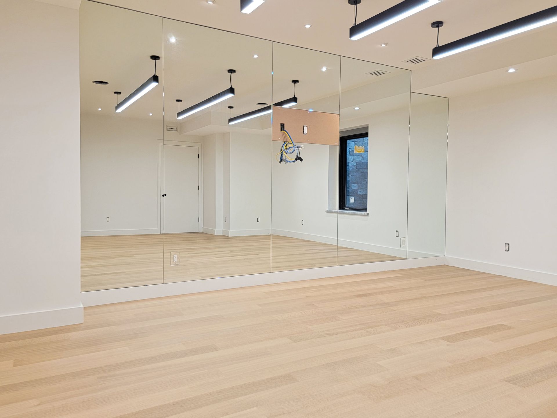 Empty dance studio with mirrored walls, hardwood floor, and overhead lights.