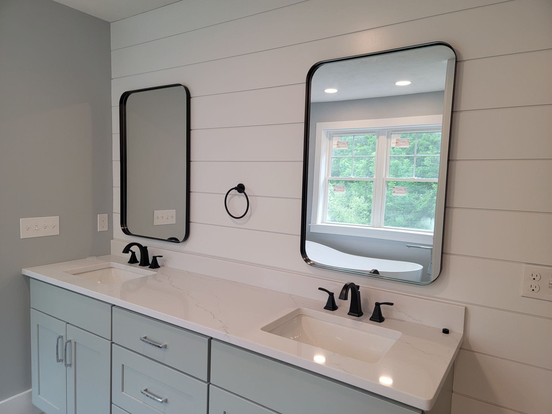 Bathroom with white countertop, gray cabinets, two black-framed mirrors, and shiplap wall.