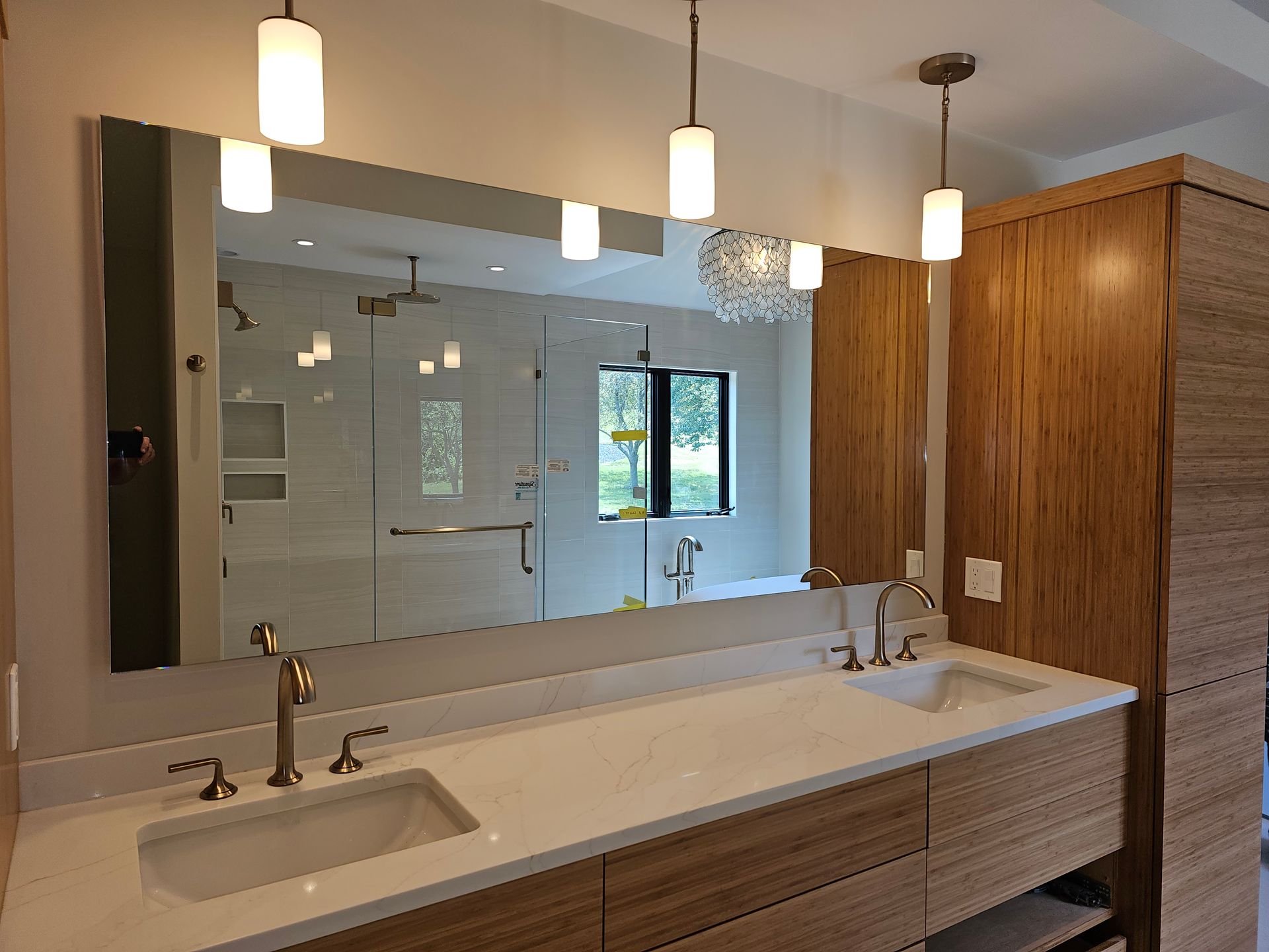 Modern bathroom with long mirror over a double sink vanity, pendant lights, and wooden cabinets.