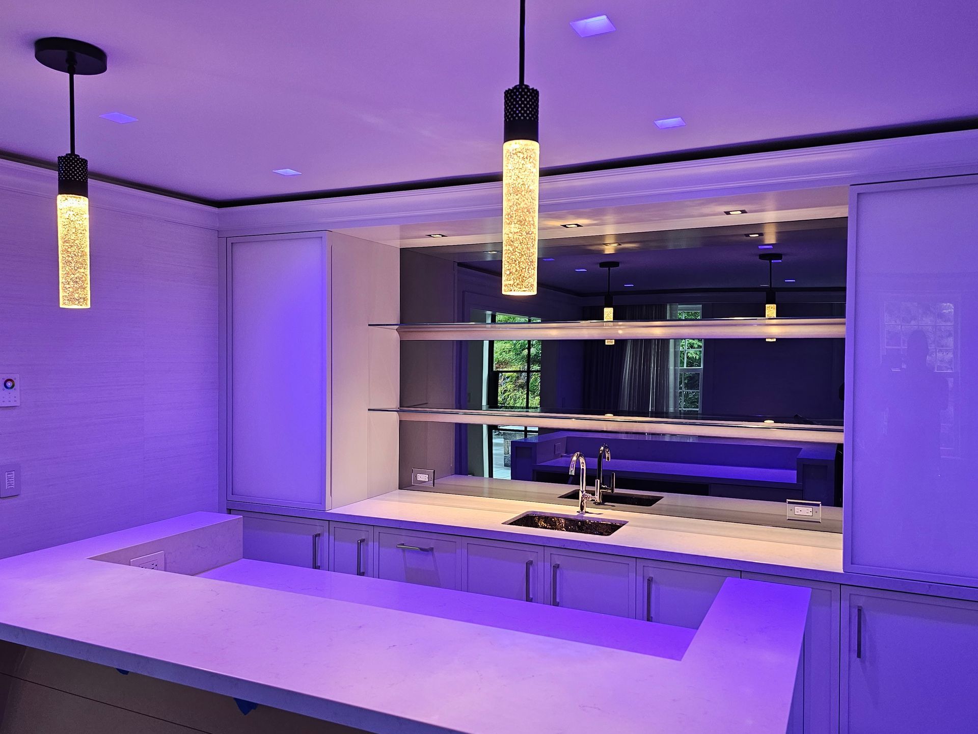 Interior bar with white countertop, mirrored back, pendant lights, and purple lighting.