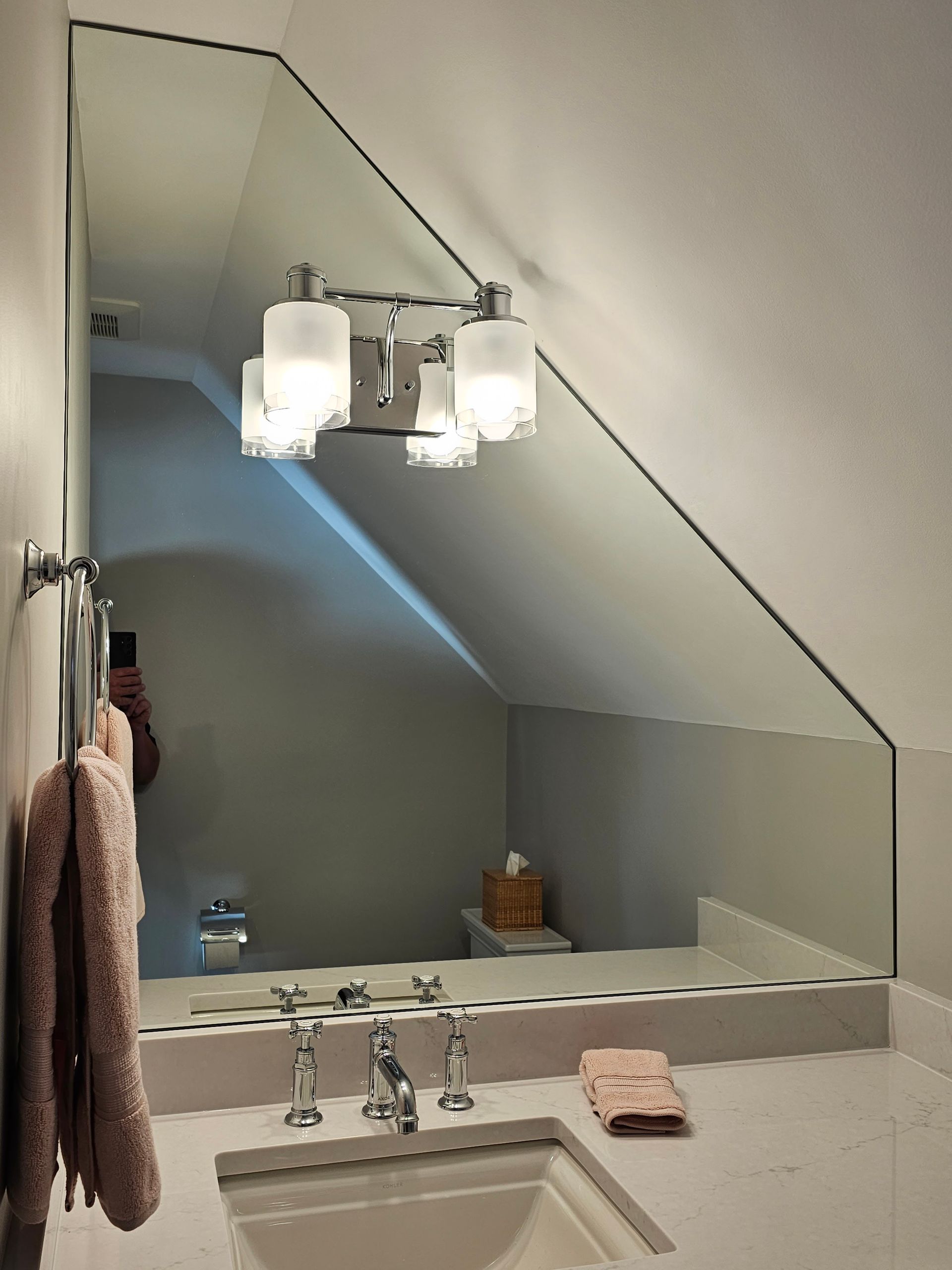 Bathroom vanity with angled mirror, sconce lighting, sink, and towels.