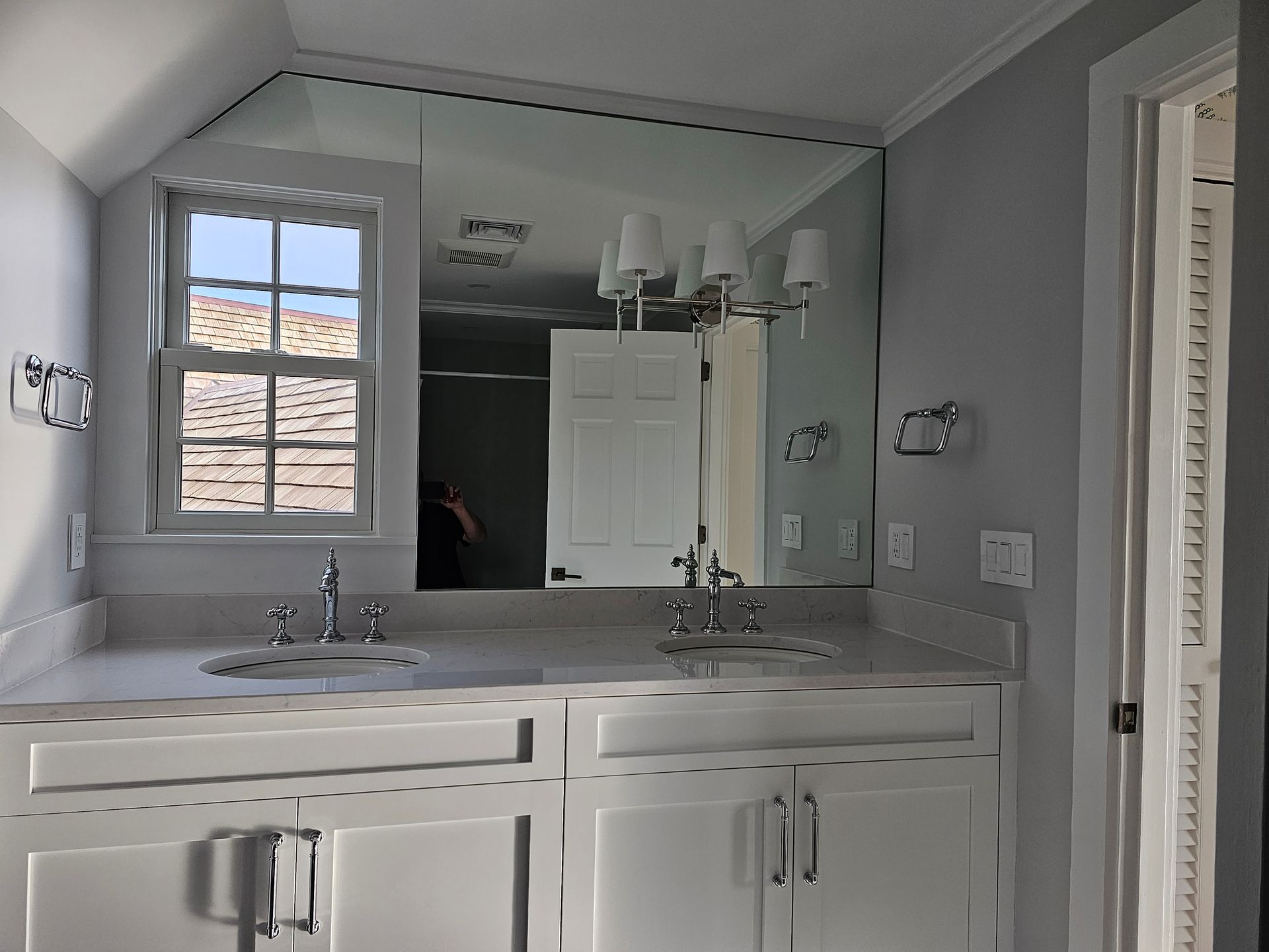 White bathroom with double sinks, large mirror, window, and door.