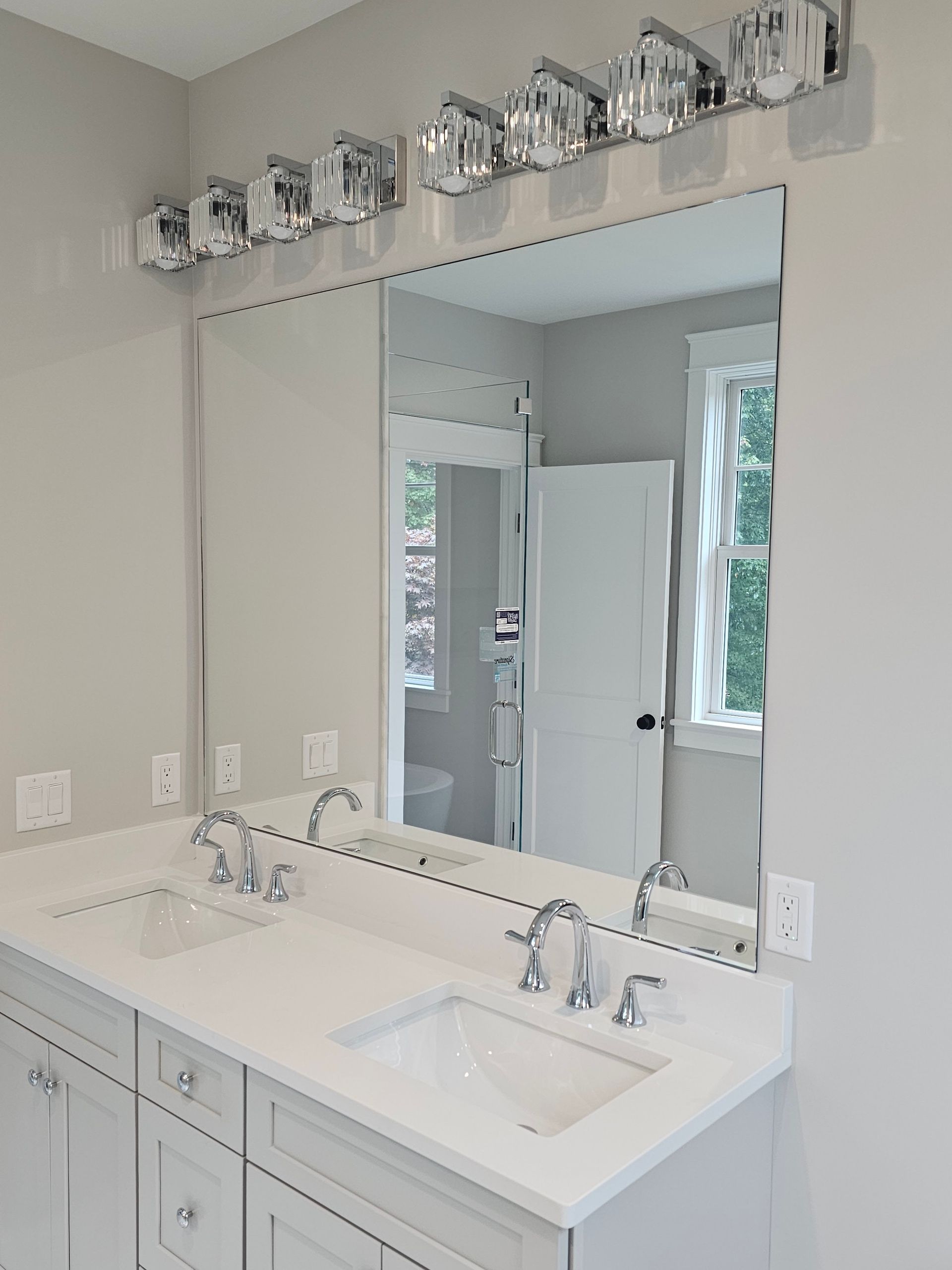 Bathroom with a large mirror above a double sink vanity, silver light fixtures.