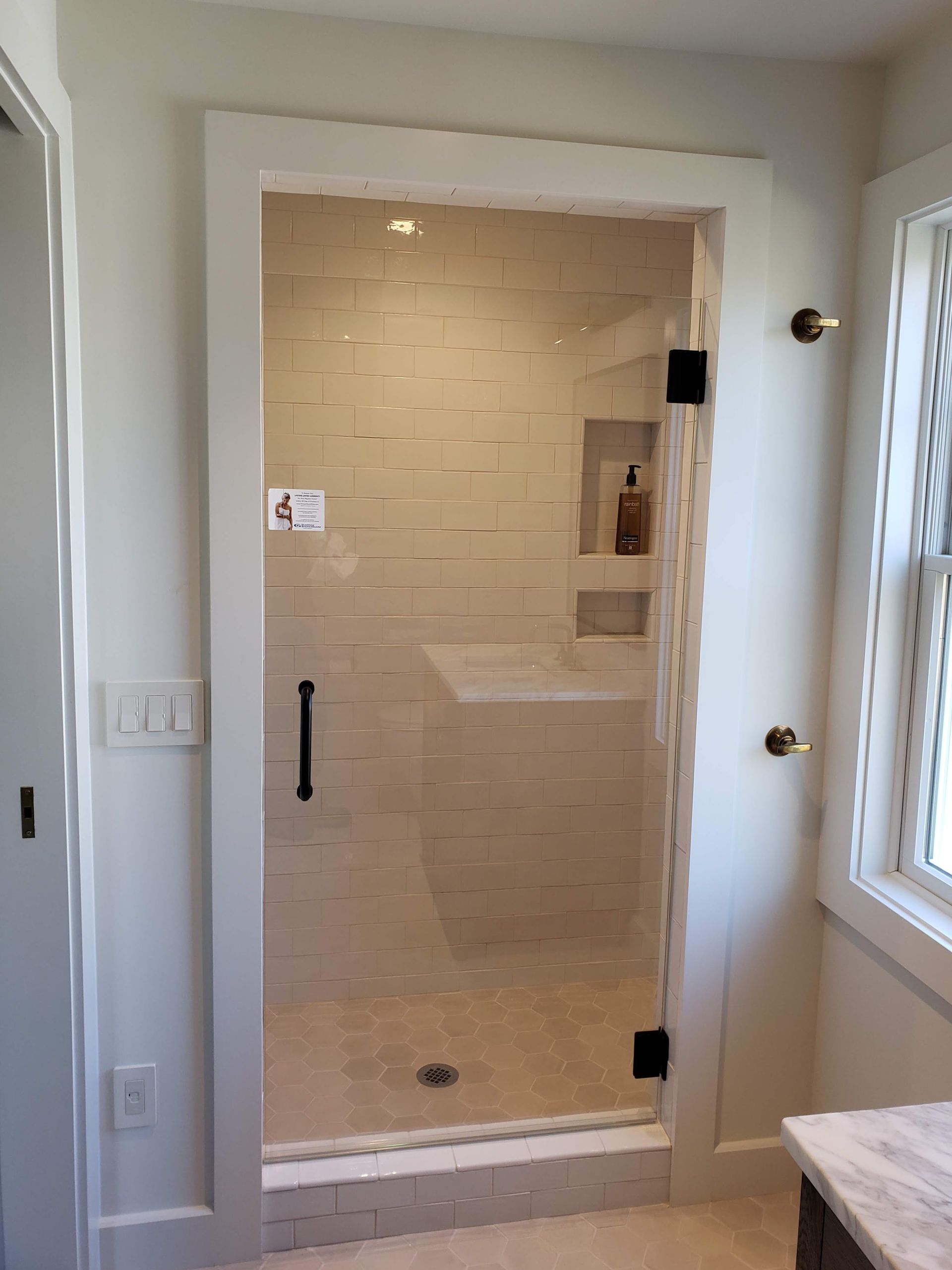 Glass shower door with black hardware, white frame, and tiled interior.