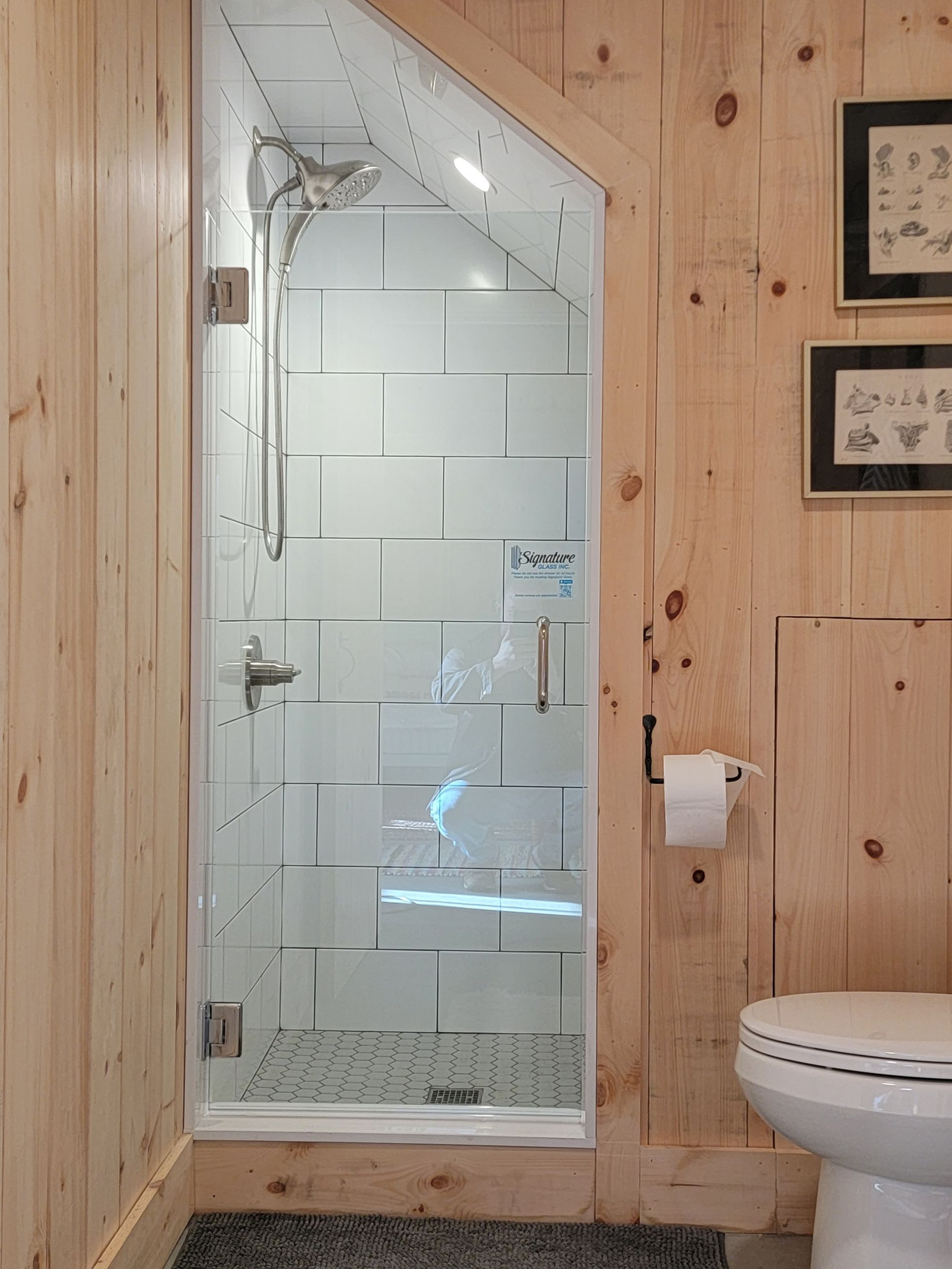 Small bathroom with light wood paneling, glass shower enclosure, white subway tiles, and toilet.
