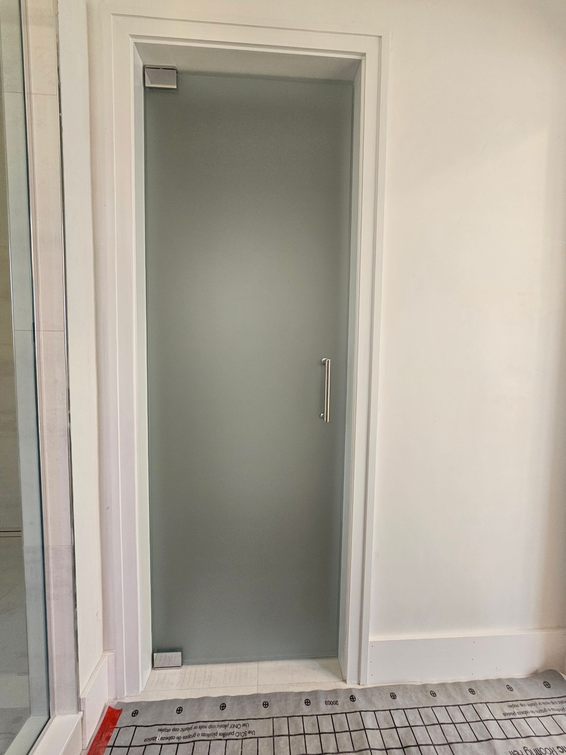 Frosted glass shower door in a white-walled bathroom, with a silver handle and a tile floor.