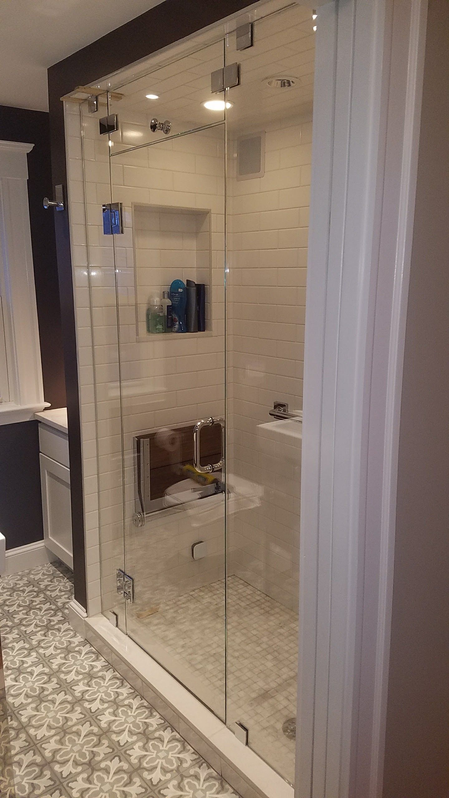 Glass shower enclosure with white tile interior, built-in shelf, and decorative flooring.