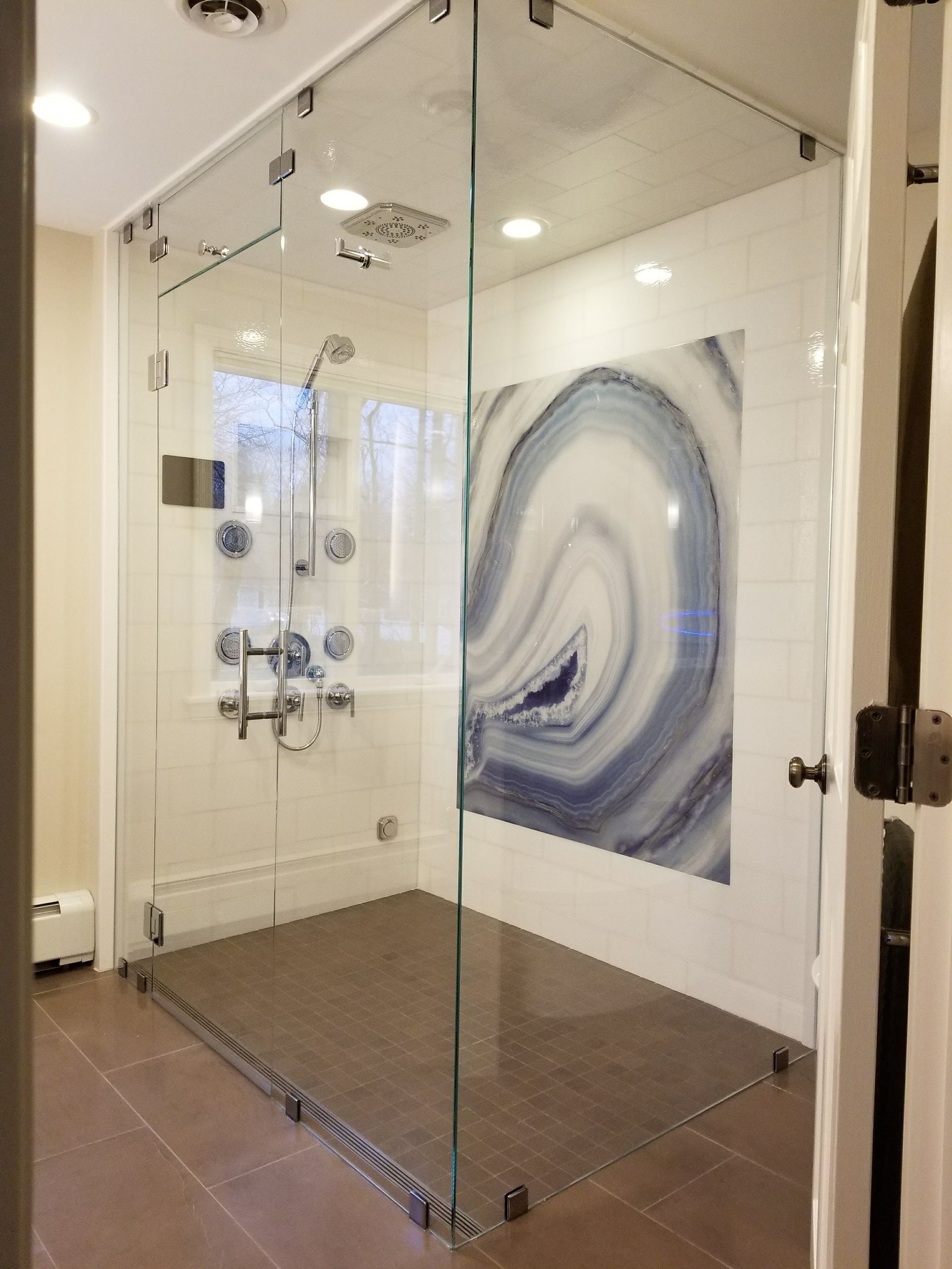 Glass shower enclosure with mosaic floor and wall art.