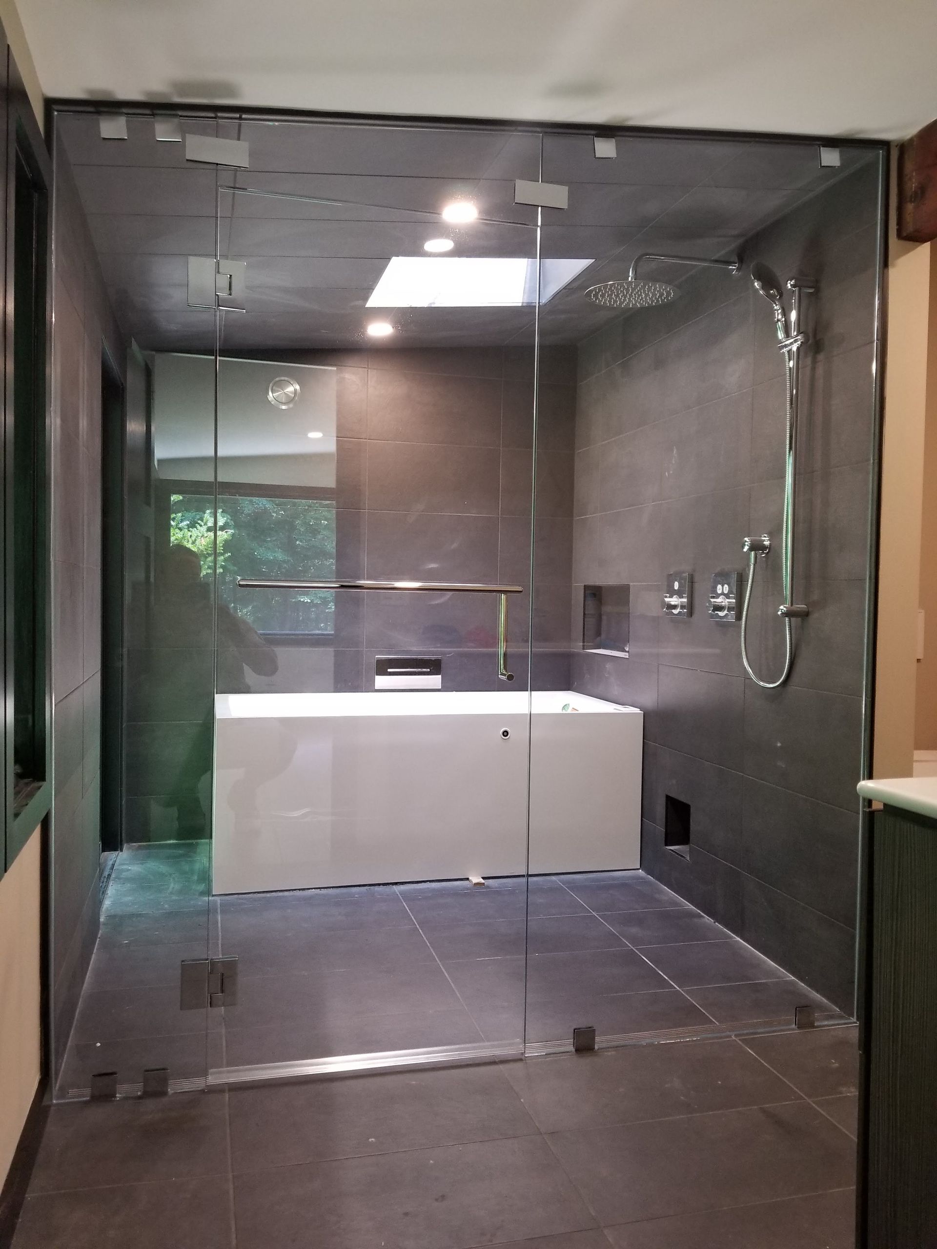 Modern bathroom with glass shower enclosure, soaking tub, dark tile walls, skylight.