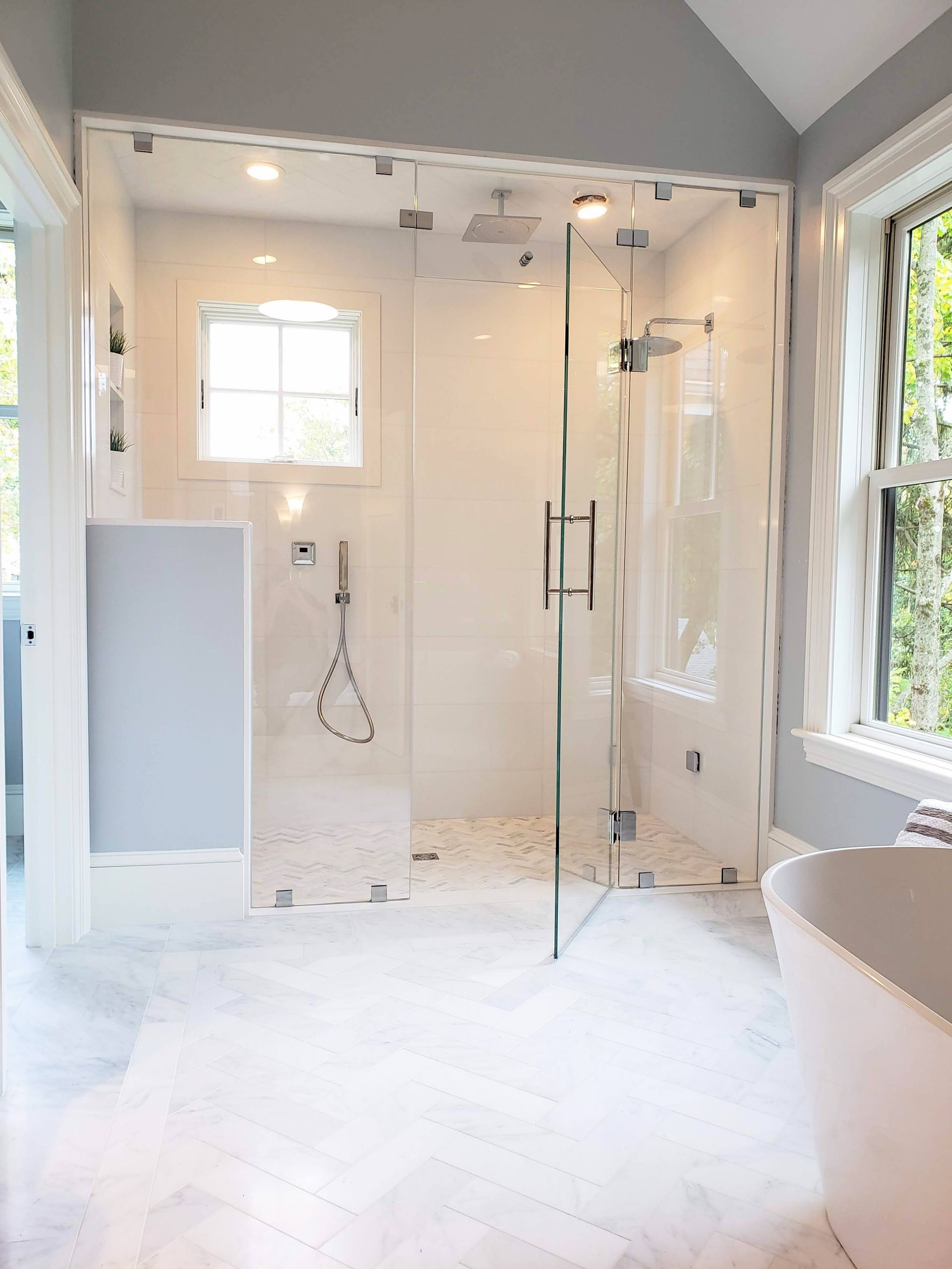 Modern bathroom with a glass-enclosed shower, white tile floor, a small window, and a bathtub partially visible.