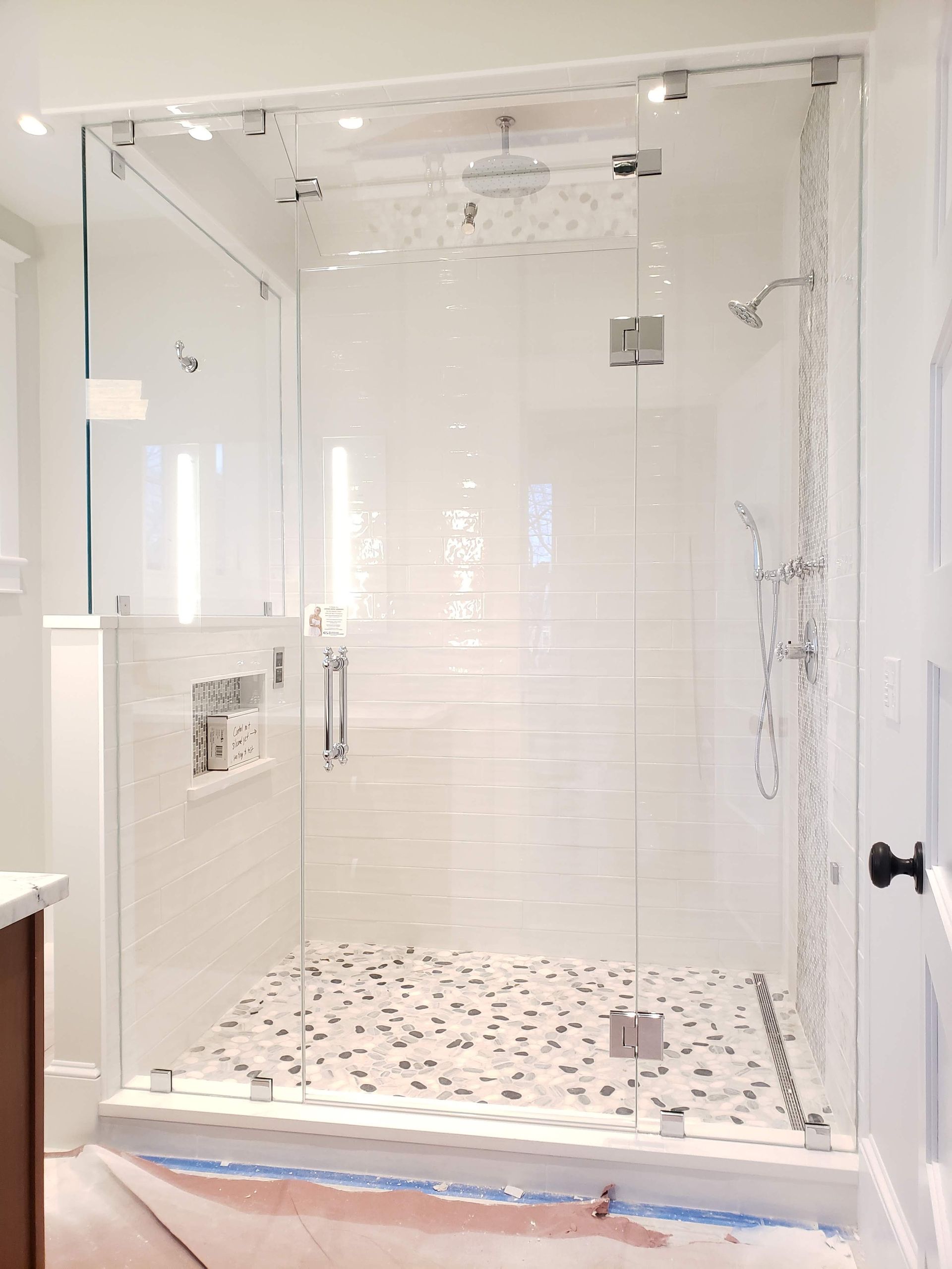 Glass shower enclosure with white tile walls and pebble floor.