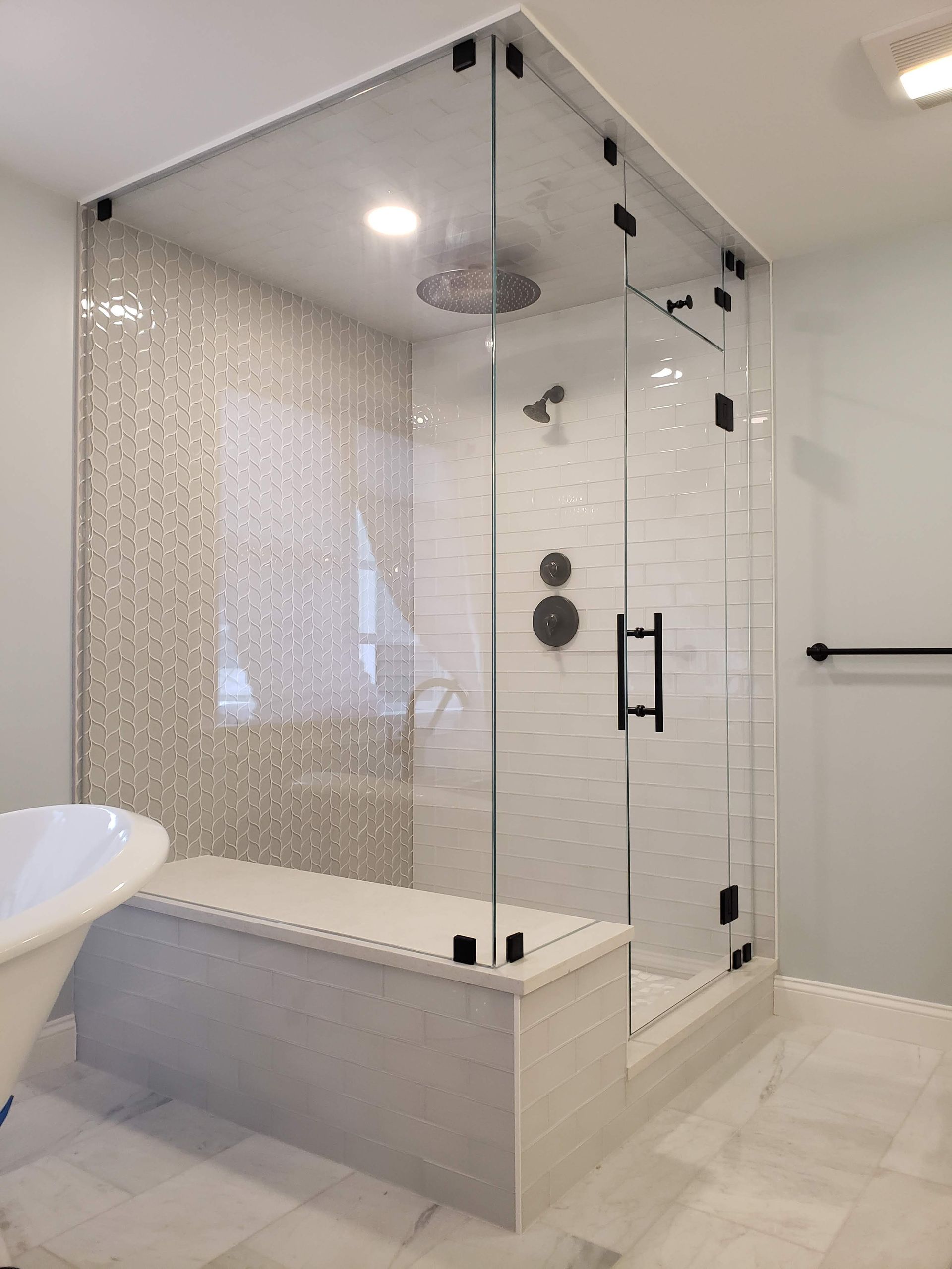 Glass shower with white tile, black hardware, and built-in bench in a modern bathroom.
