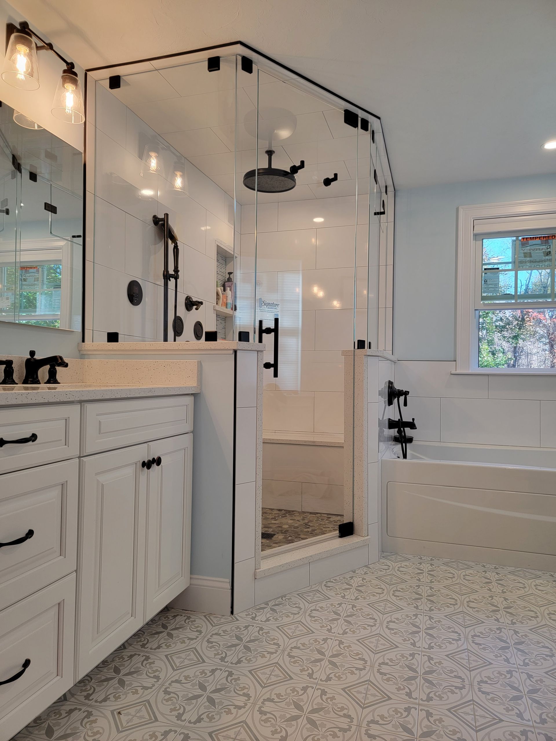 Bathroom with white vanity, glass shower, and soaking tub. Light blue walls, black fixtures, and patterned floor.