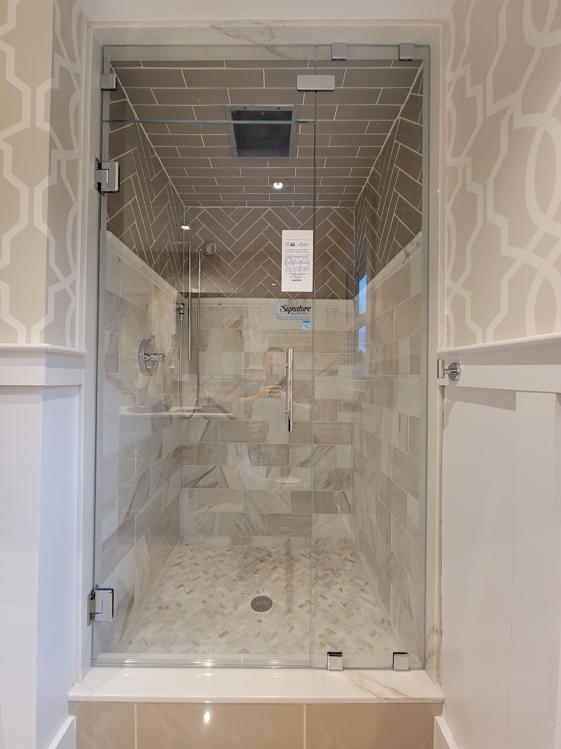 Glass shower with tile walls, marble floor, and decorative patterned wallpaper.