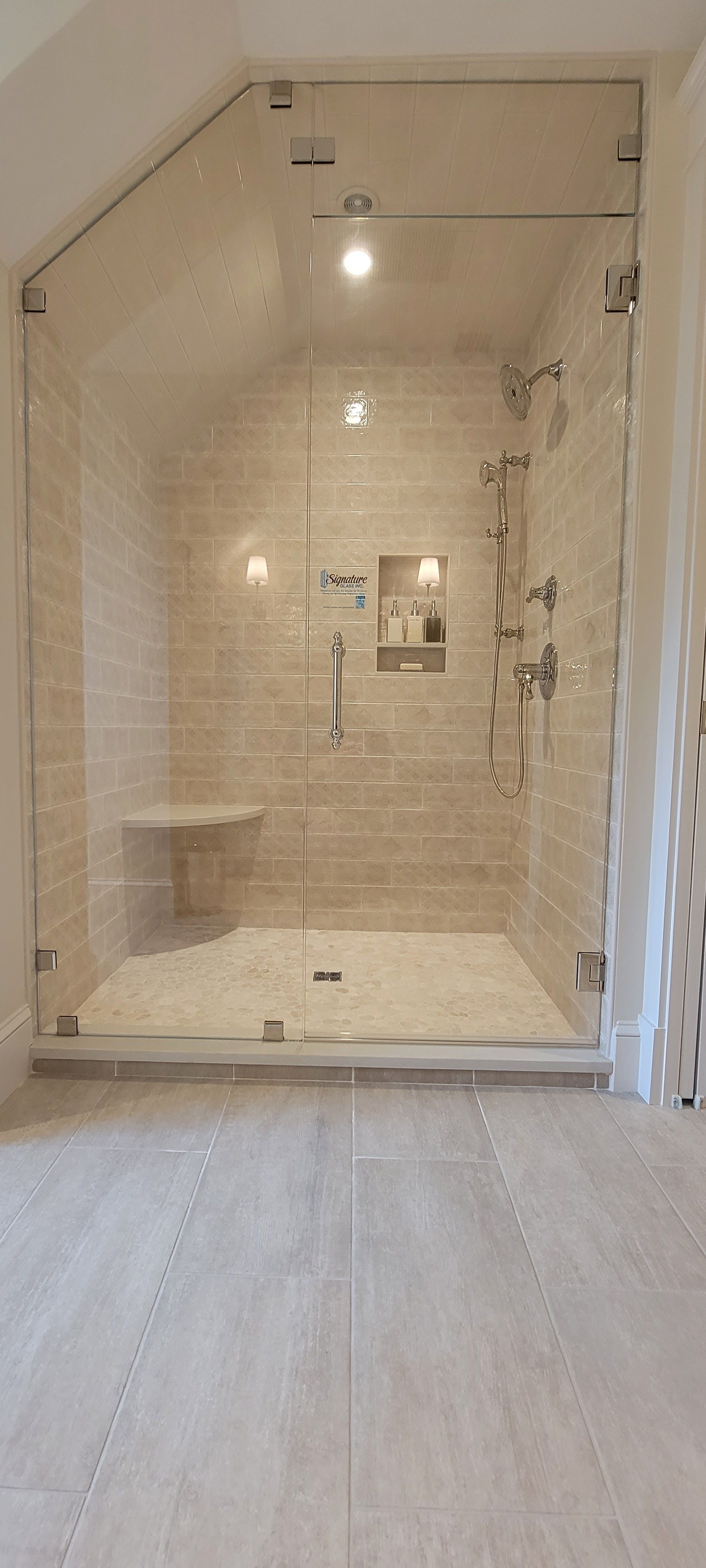 A glass-enclosed shower in a modern bathroom. It has light-colored tile and a built-in bench.