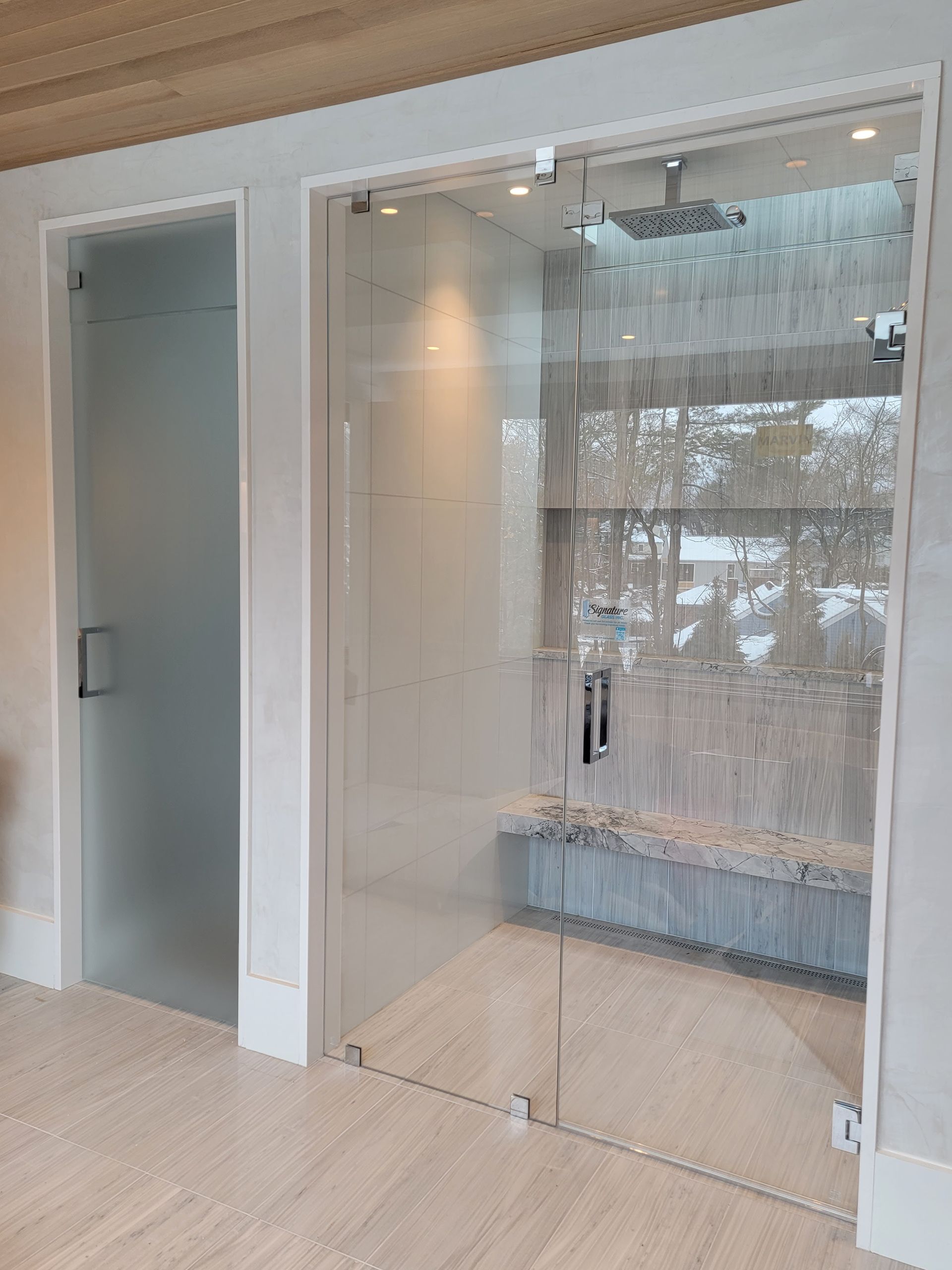 Two glass shower doors, one frosted, next to each other. White walls, light floor.