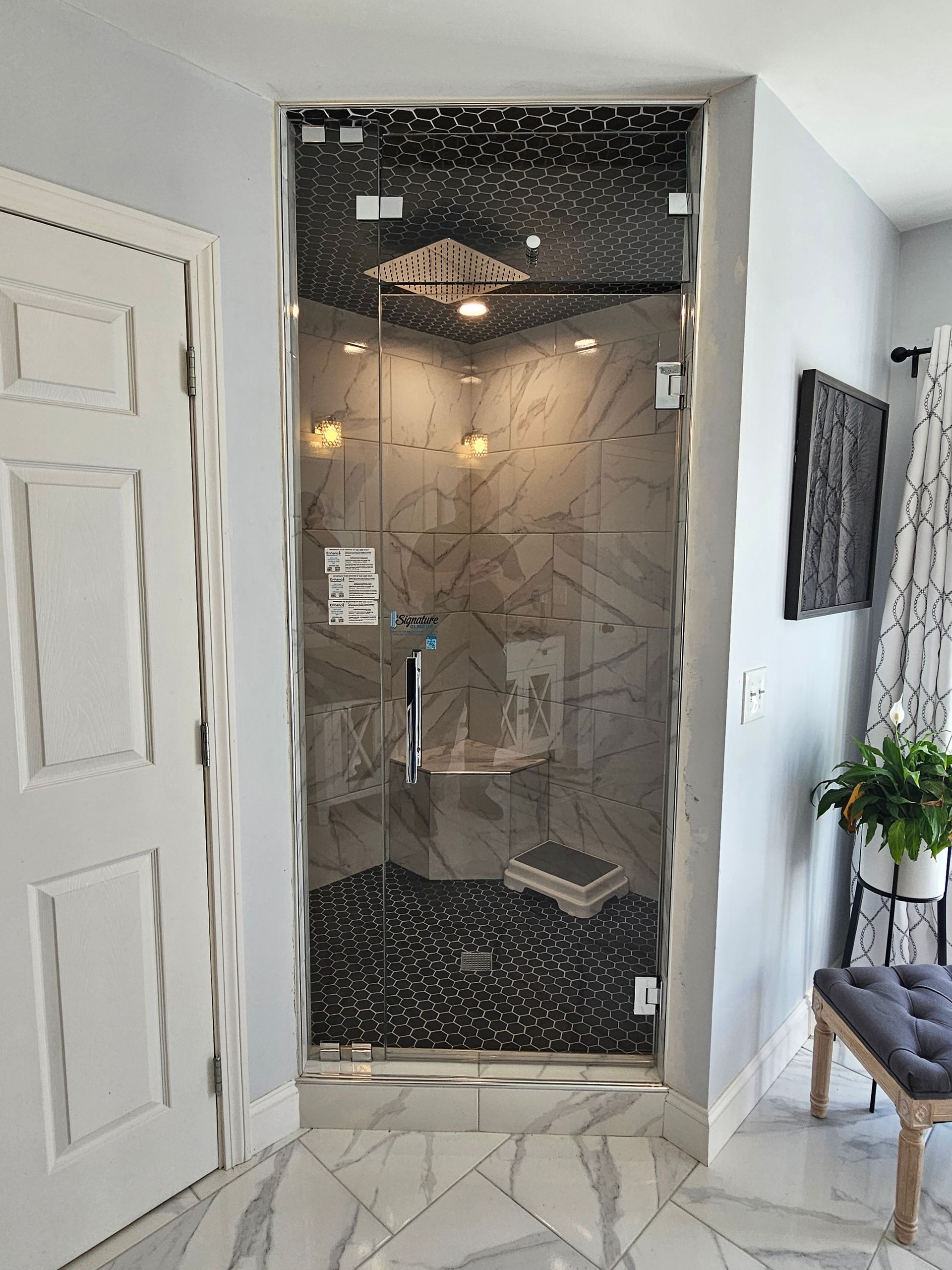Glass shower with black and gray marble tiles, stone floor, and white door on the left.