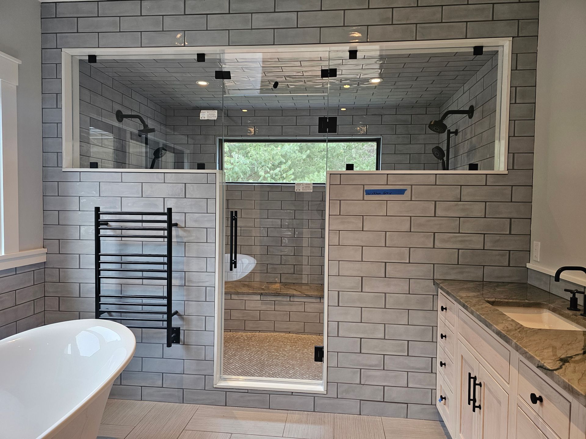 Modern bathroom with a glass-enclosed shower, freestanding tub, light gray brick tile, and a double vanity.