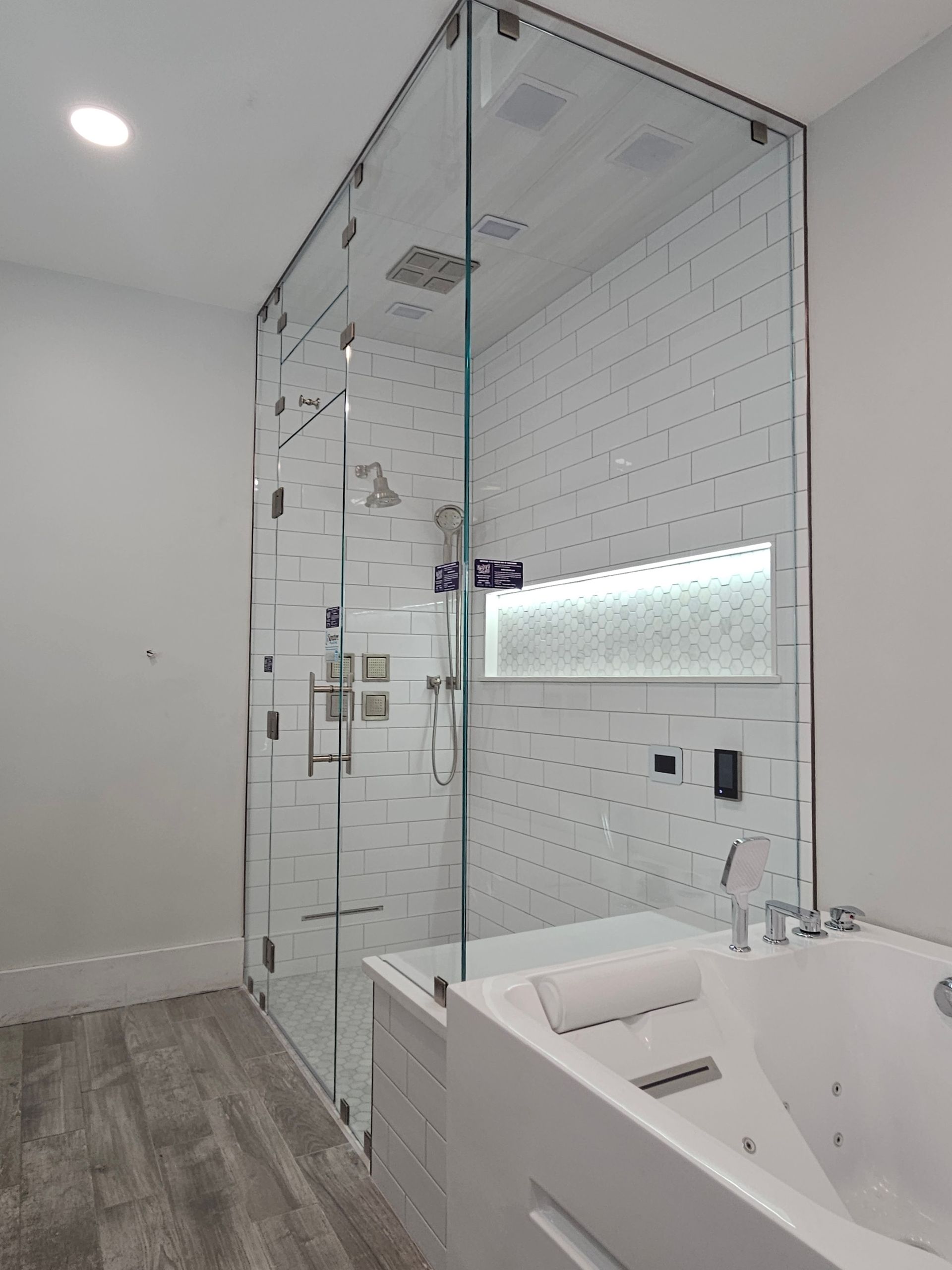 Modern glass shower enclosure with white tiled walls and a built-in tub.