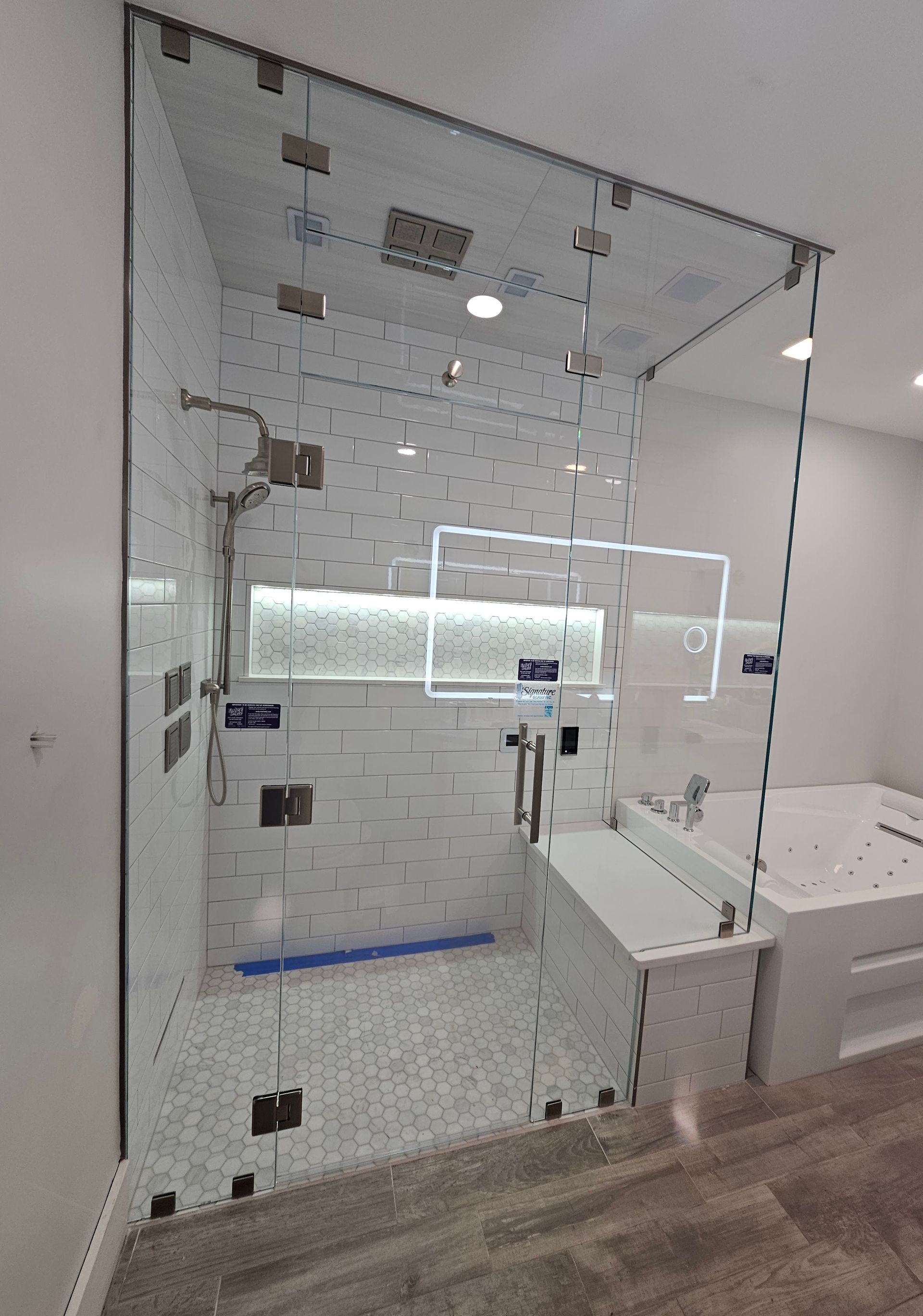 Glass shower enclosure with white tile interior, silver fixtures, and a white bathtub.