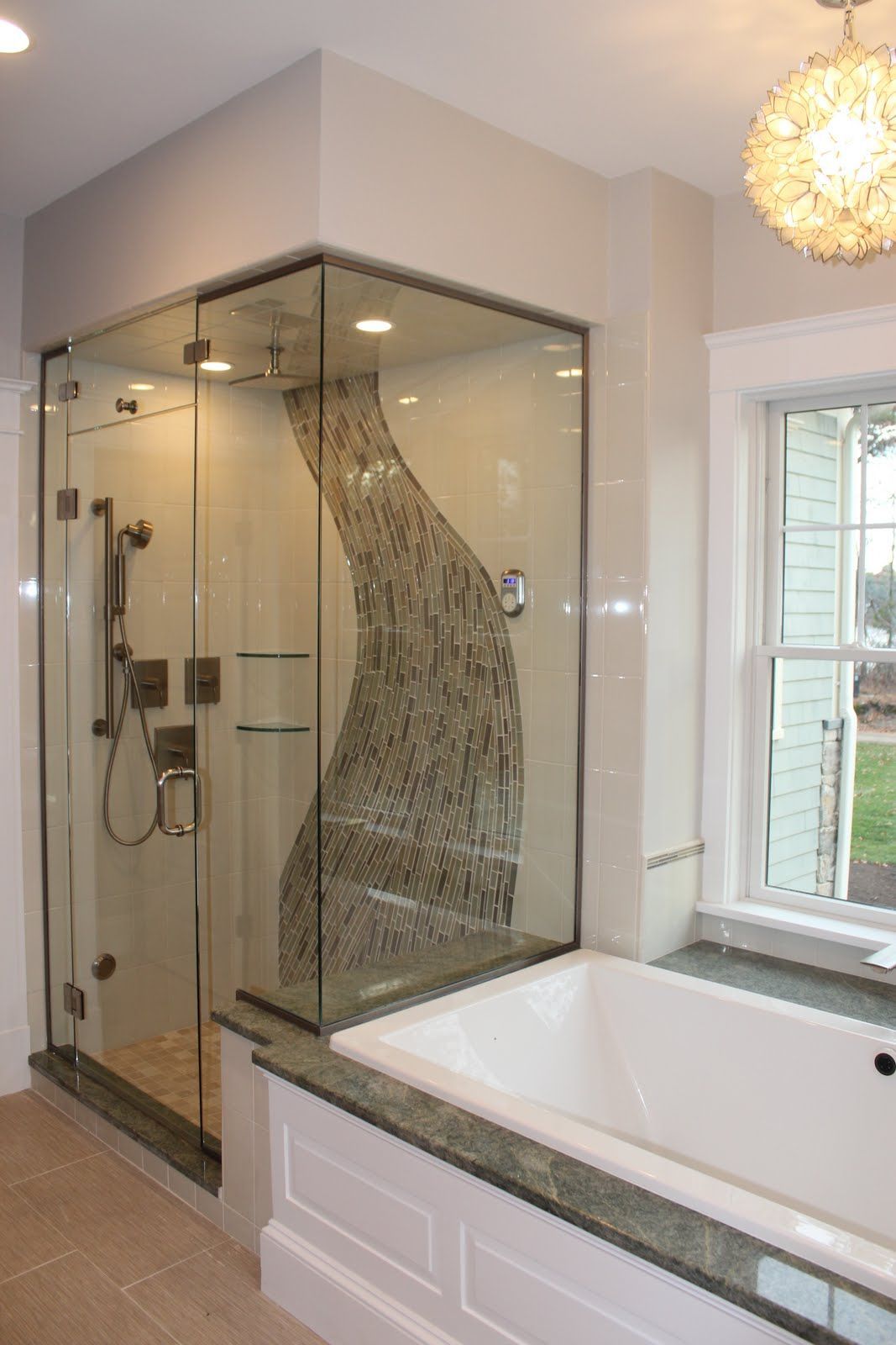 Modern bathroom with glass shower, tub, decorative stone wall. Light colors, window on the right.