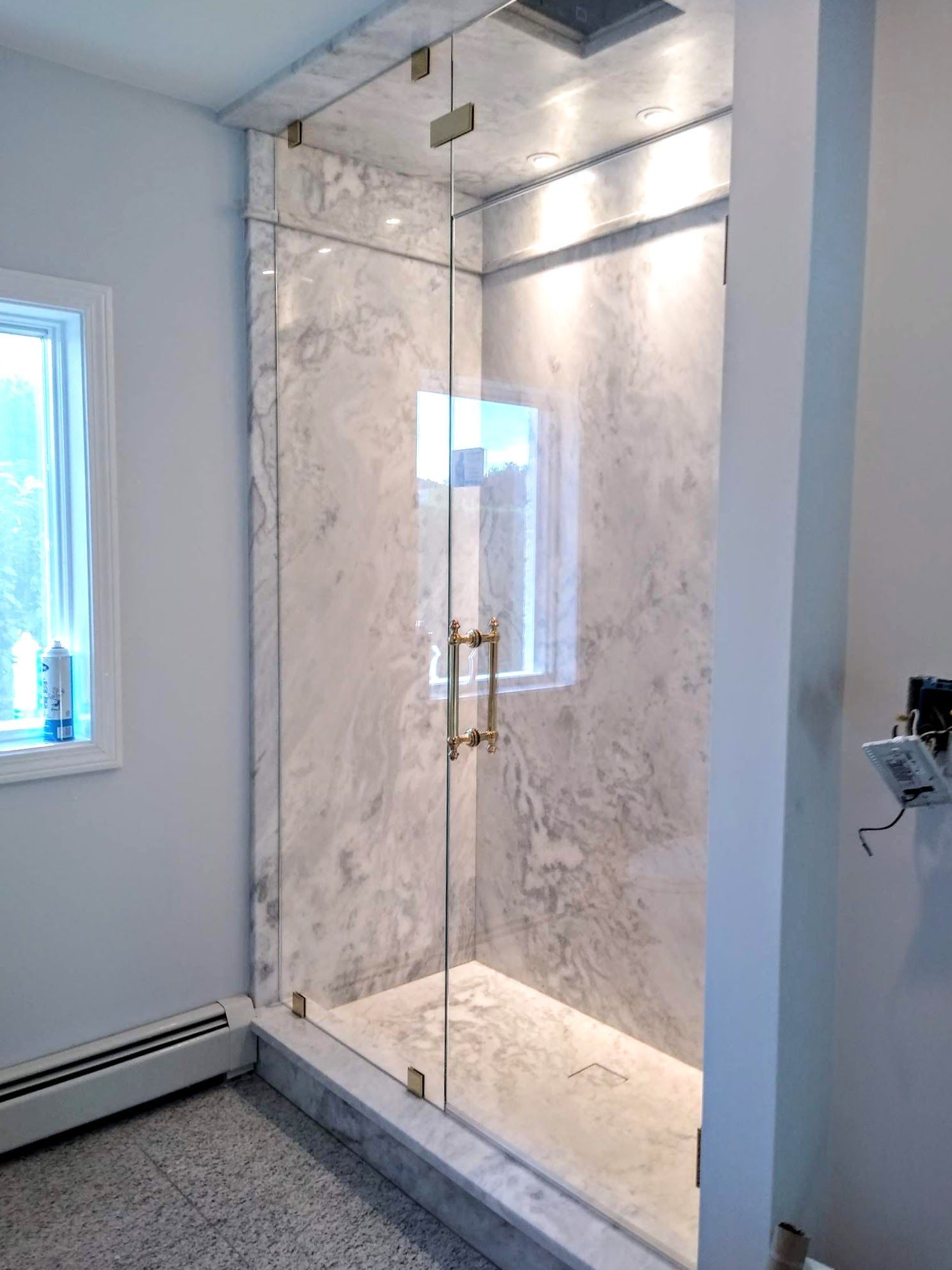 Glass shower enclosure with marble-like wall and floor in a bathroom with a window.
