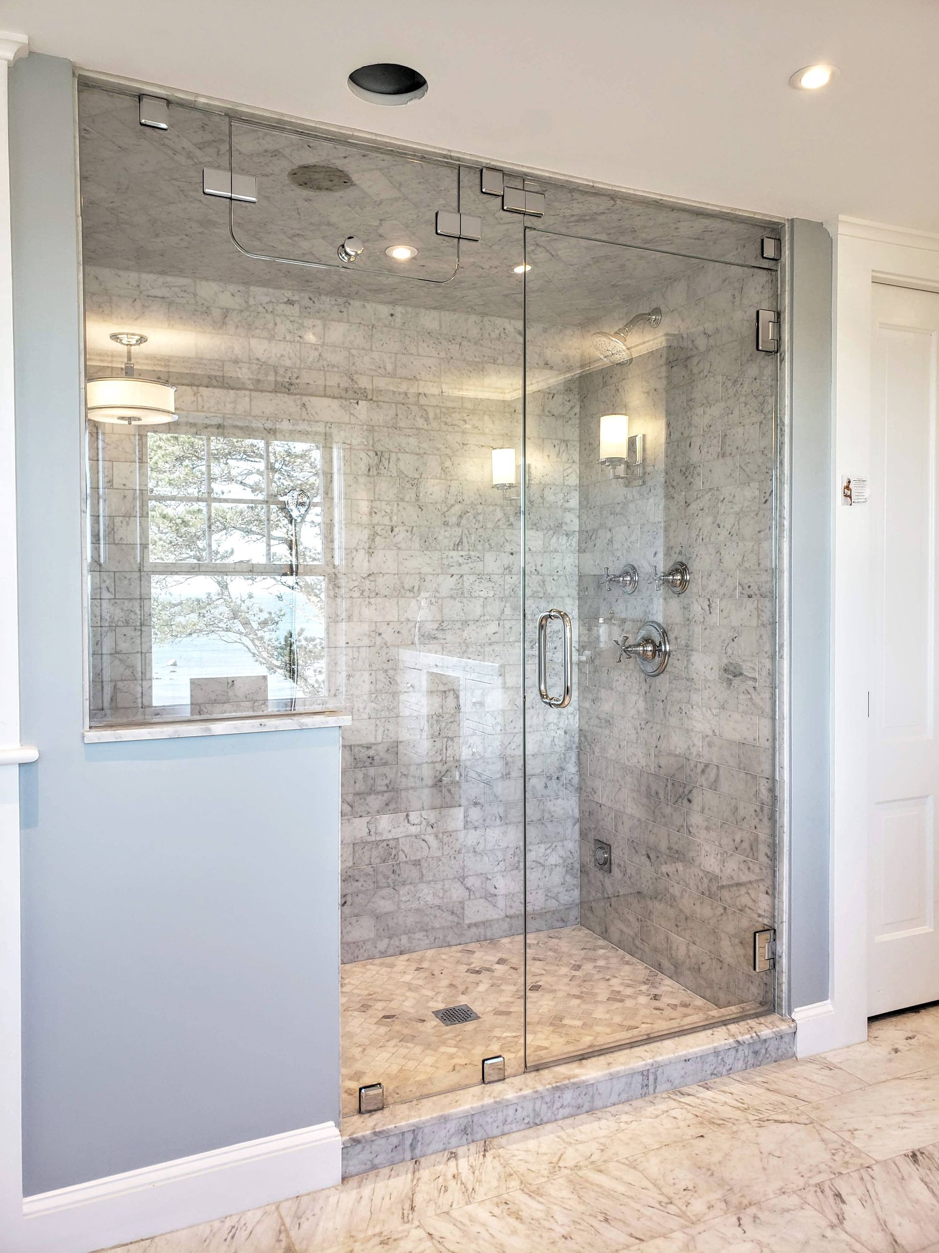 Glass-walled shower with marble tile, silver fixtures, and a glass door. Interior shot of a bathroom.