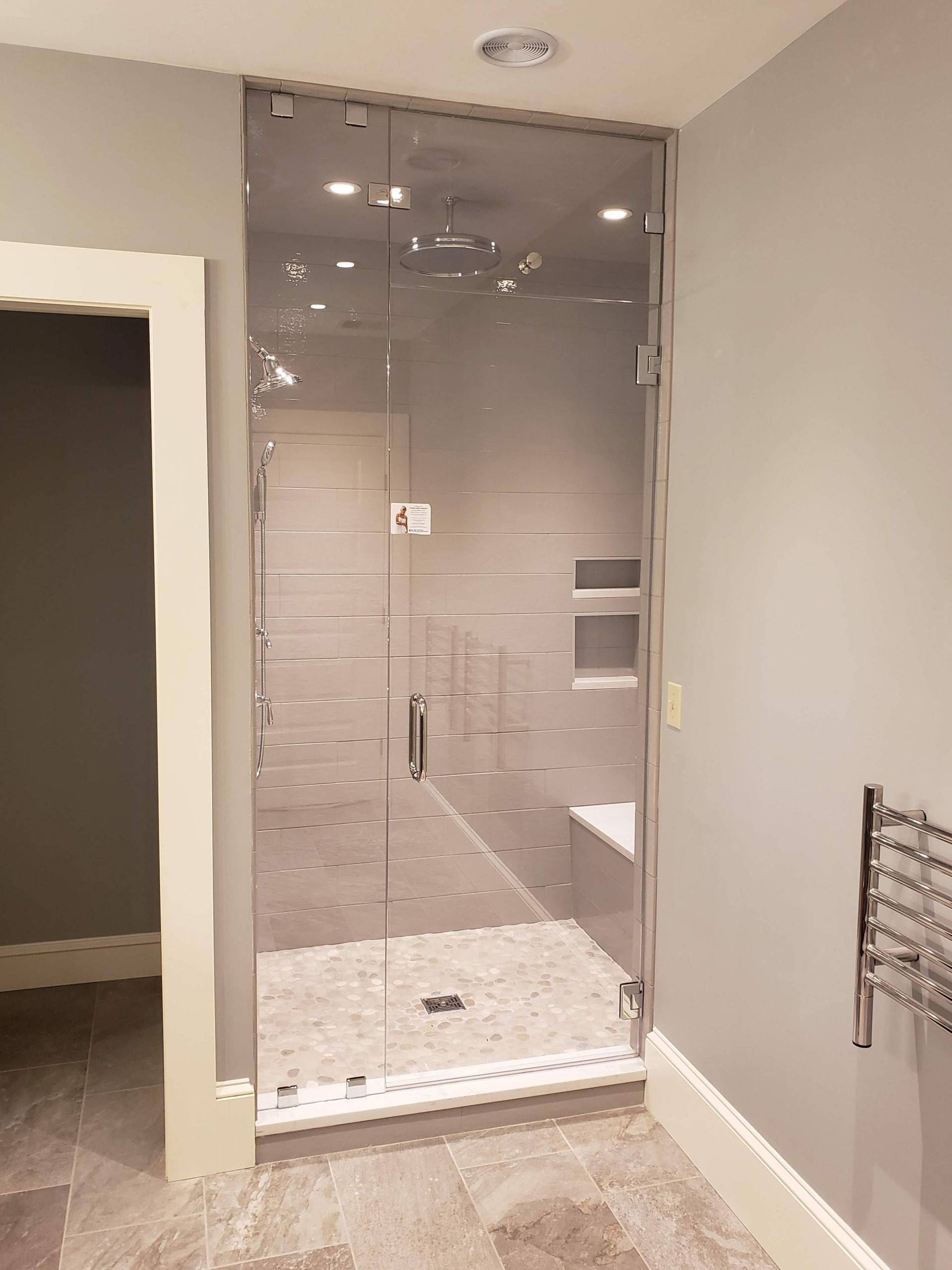 Glass shower enclosure in a gray-walled bathroom with white trim and a heated towel rack.