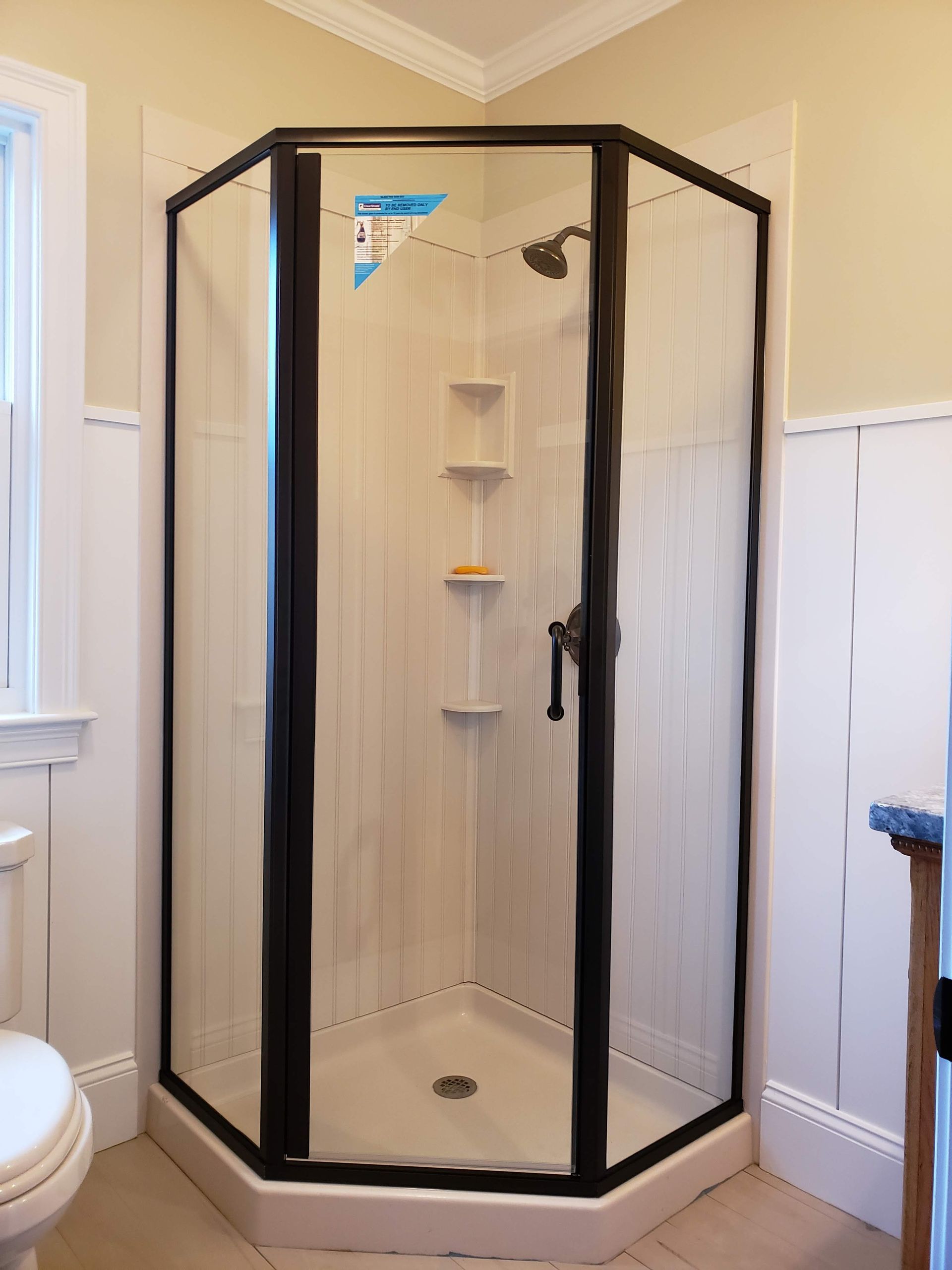 Black-framed, octagonal shower stall with white walls and shelves, set in a light-yellow bathroom.