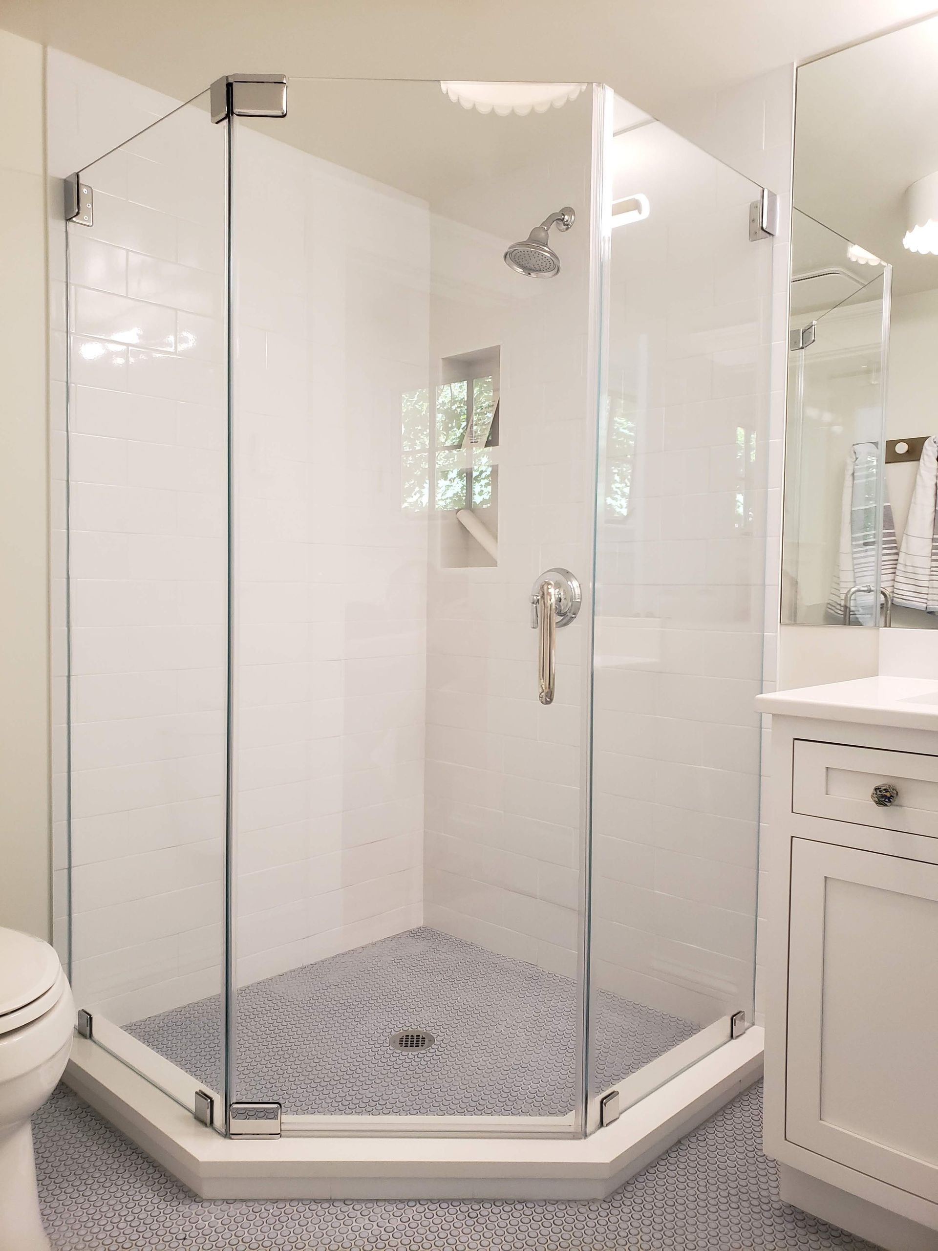 Glass-enclosed shower with white tiled walls and a blue-gray patterned floor. Chrome fixtures.