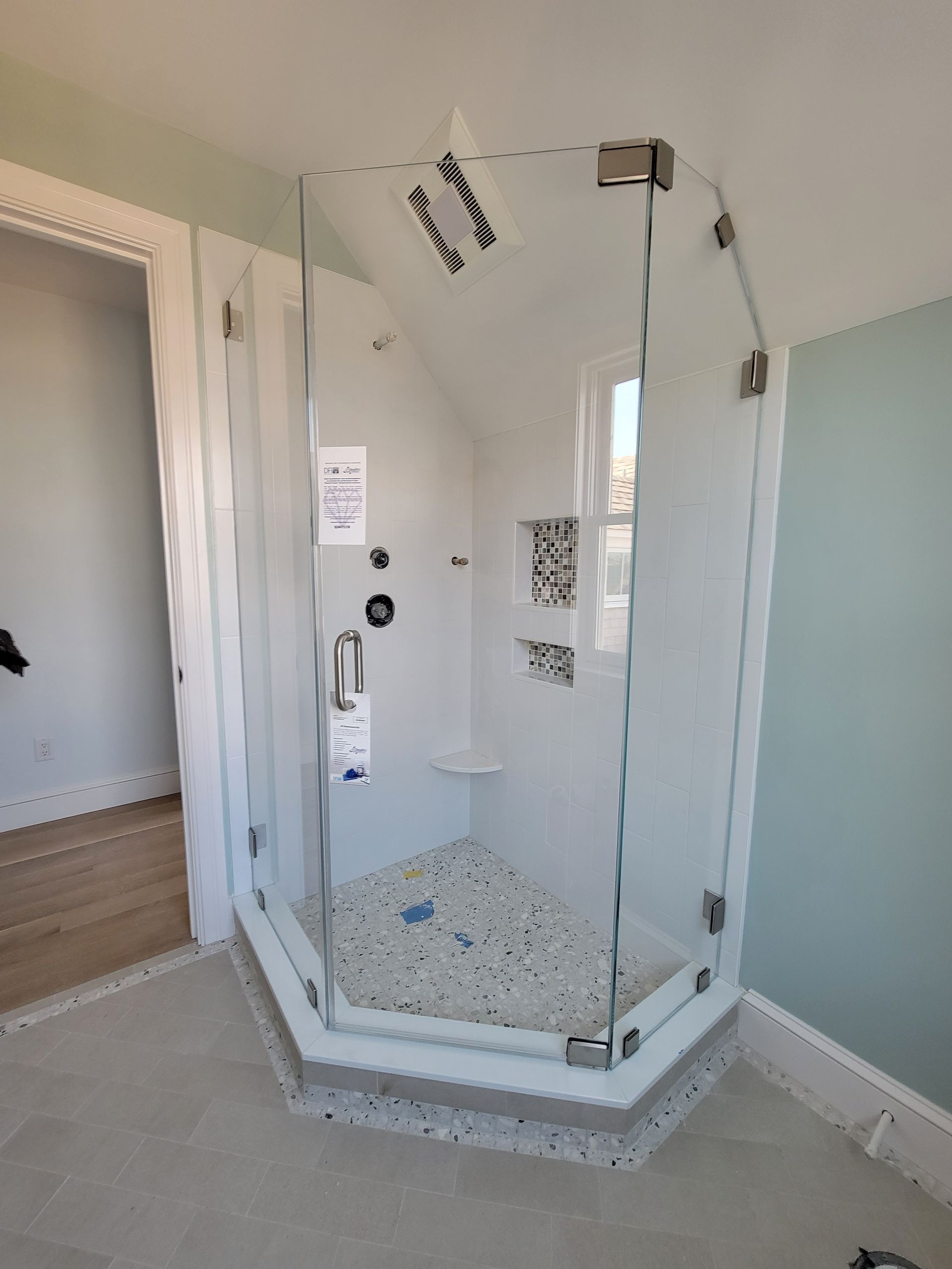 Glass shower enclosure in a bathroom, with white walls and a gray floor.