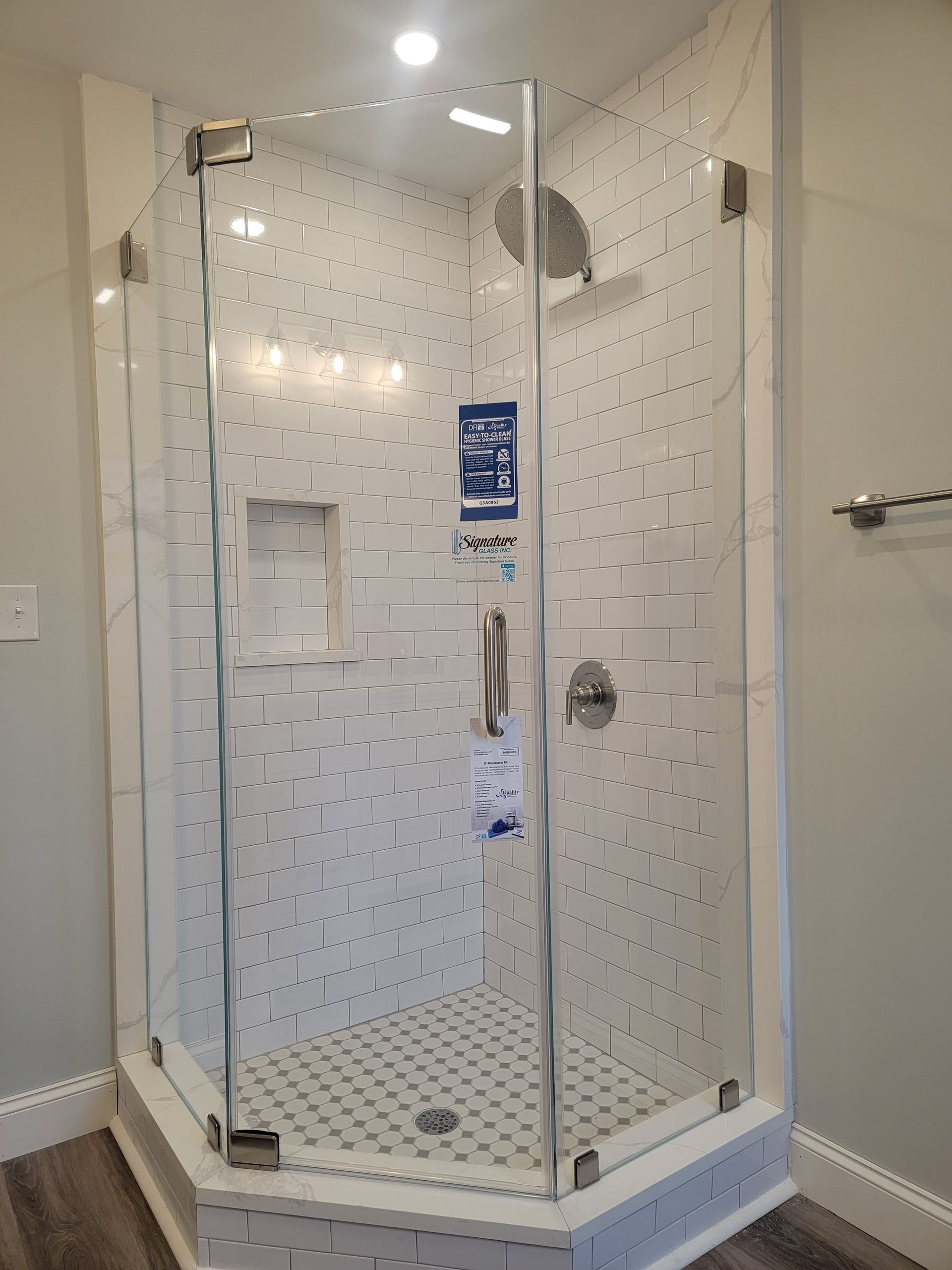Shower stall with glass doors, white tiled walls, and silver fixtures.