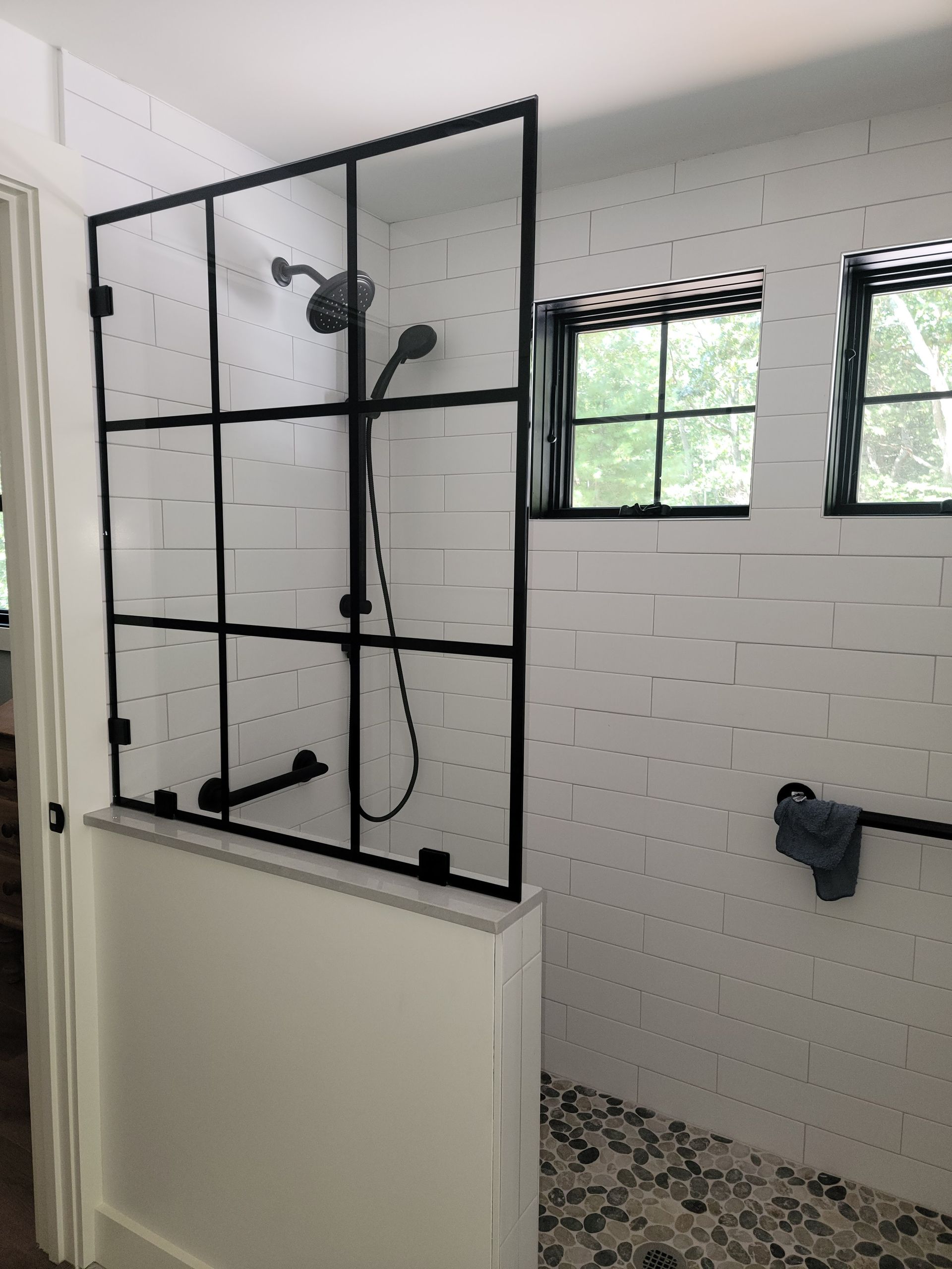 Shower stall with black framed glass door, white tile wall, and pebble floor.