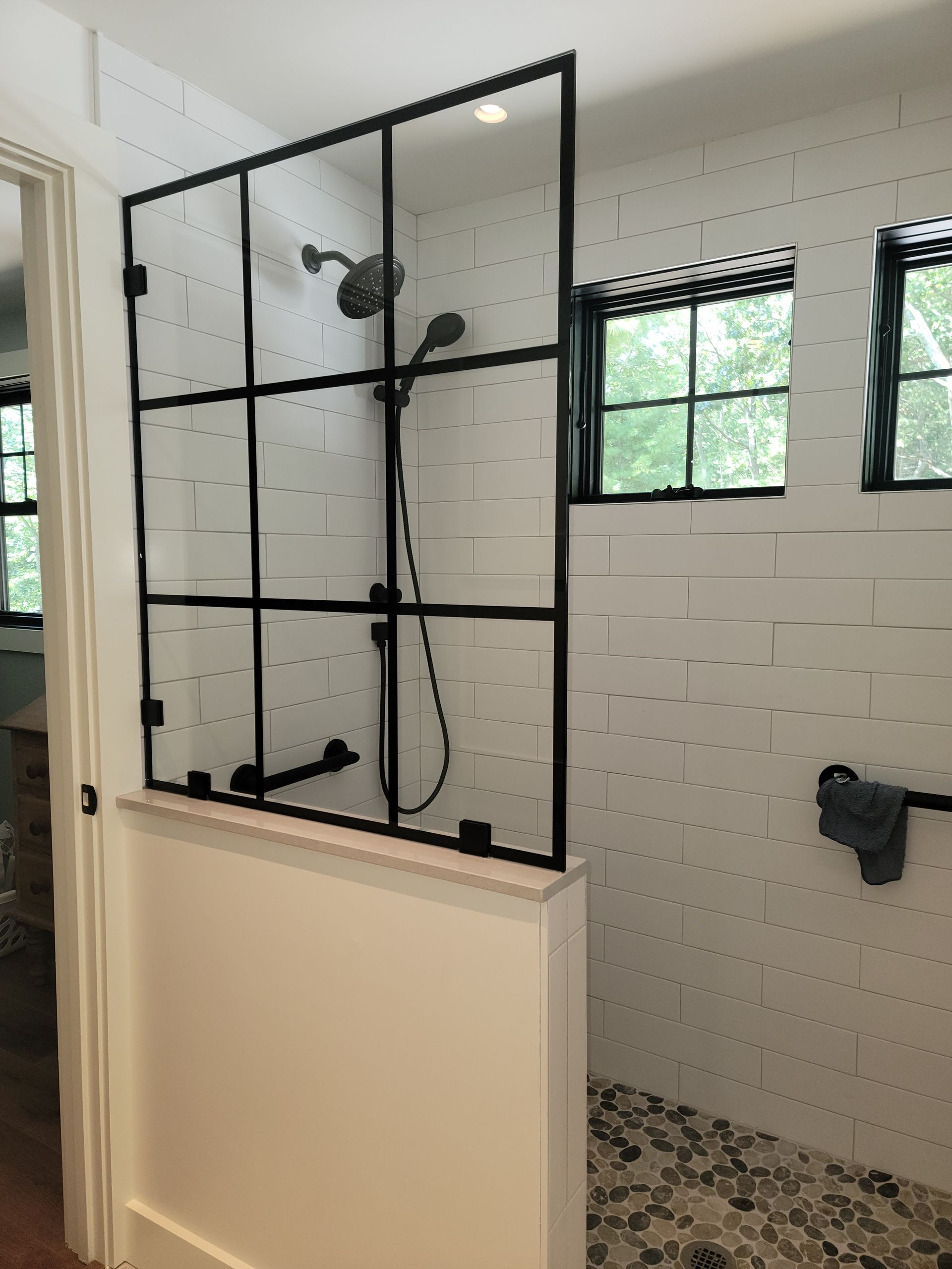 Shower with black framed glass enclosure, white tile walls, and pebble floor.