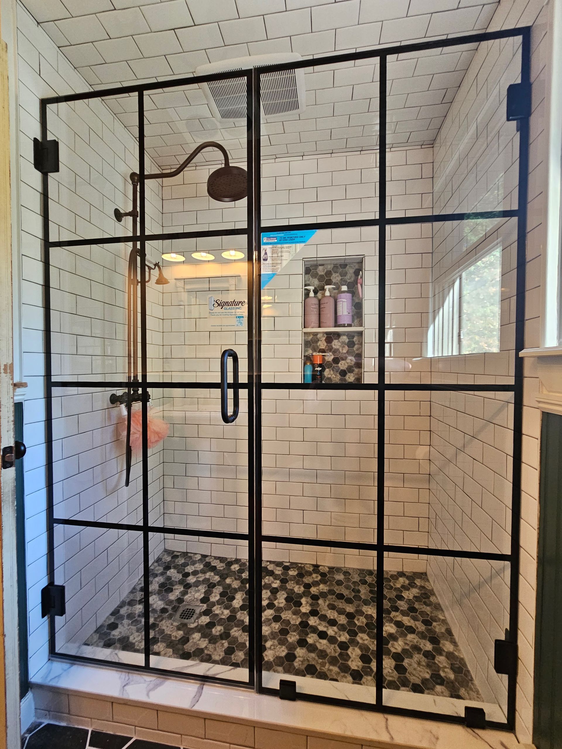Shower with black framed glass doors, white subway tile walls, and dark stone floor.