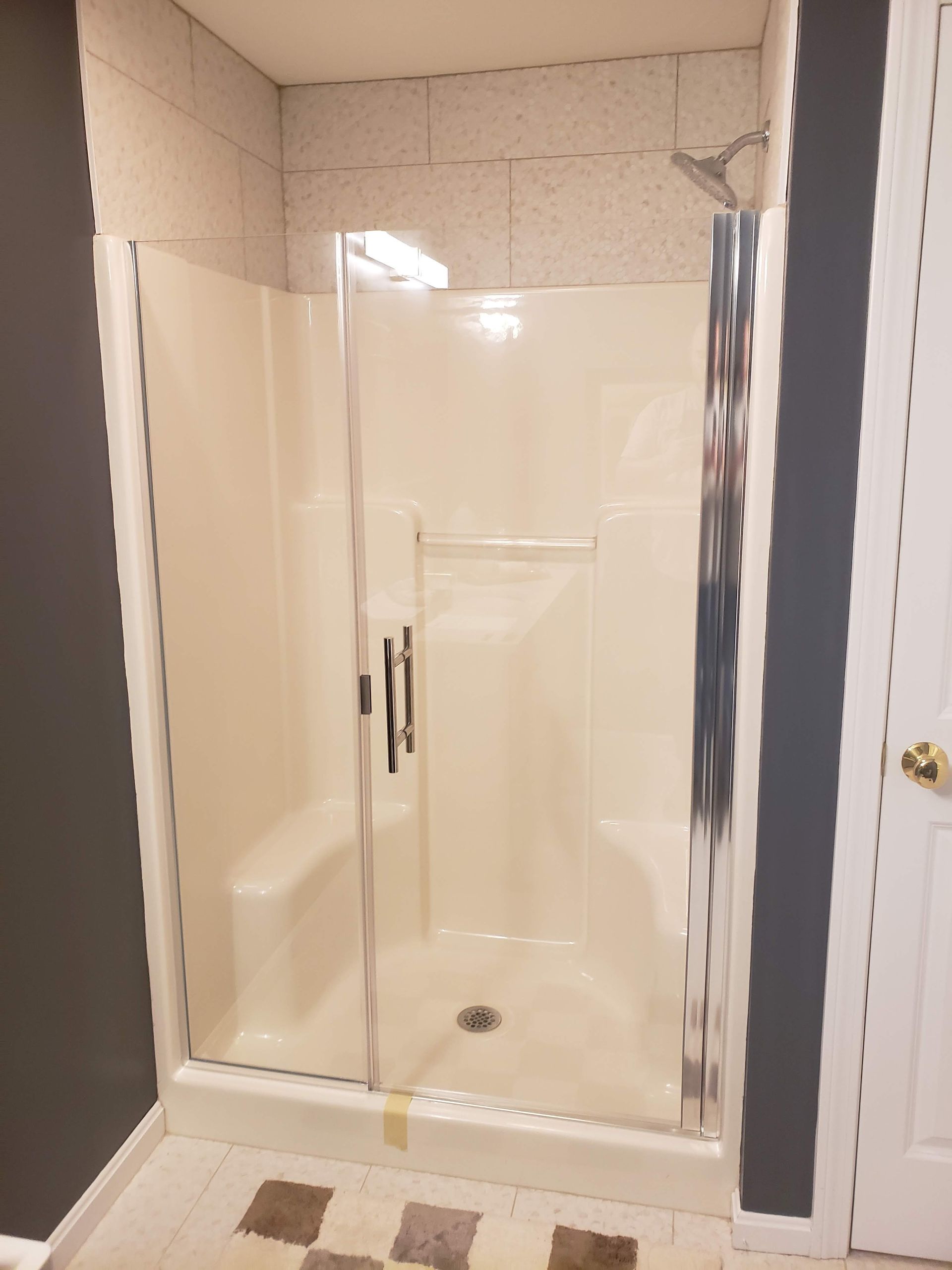 Shower stall with glass door, beige walls, chrome fixtures.