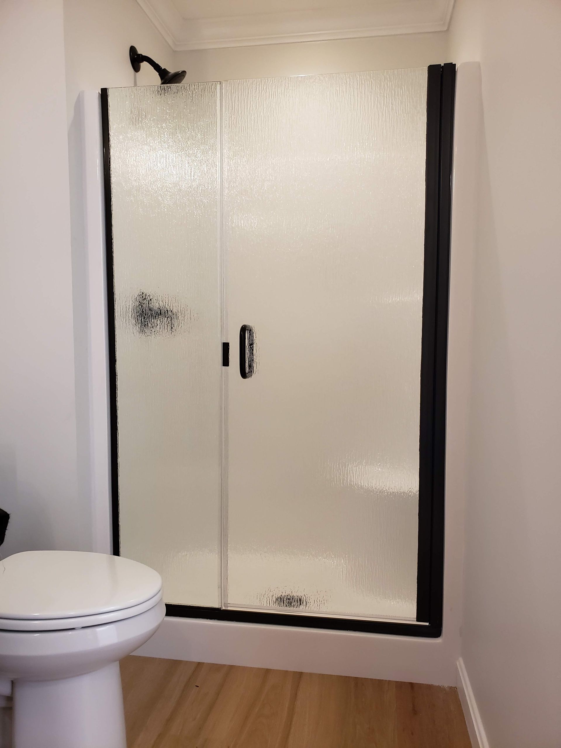 Shower with textured glass doors, black frame, and a toilet on the left.
