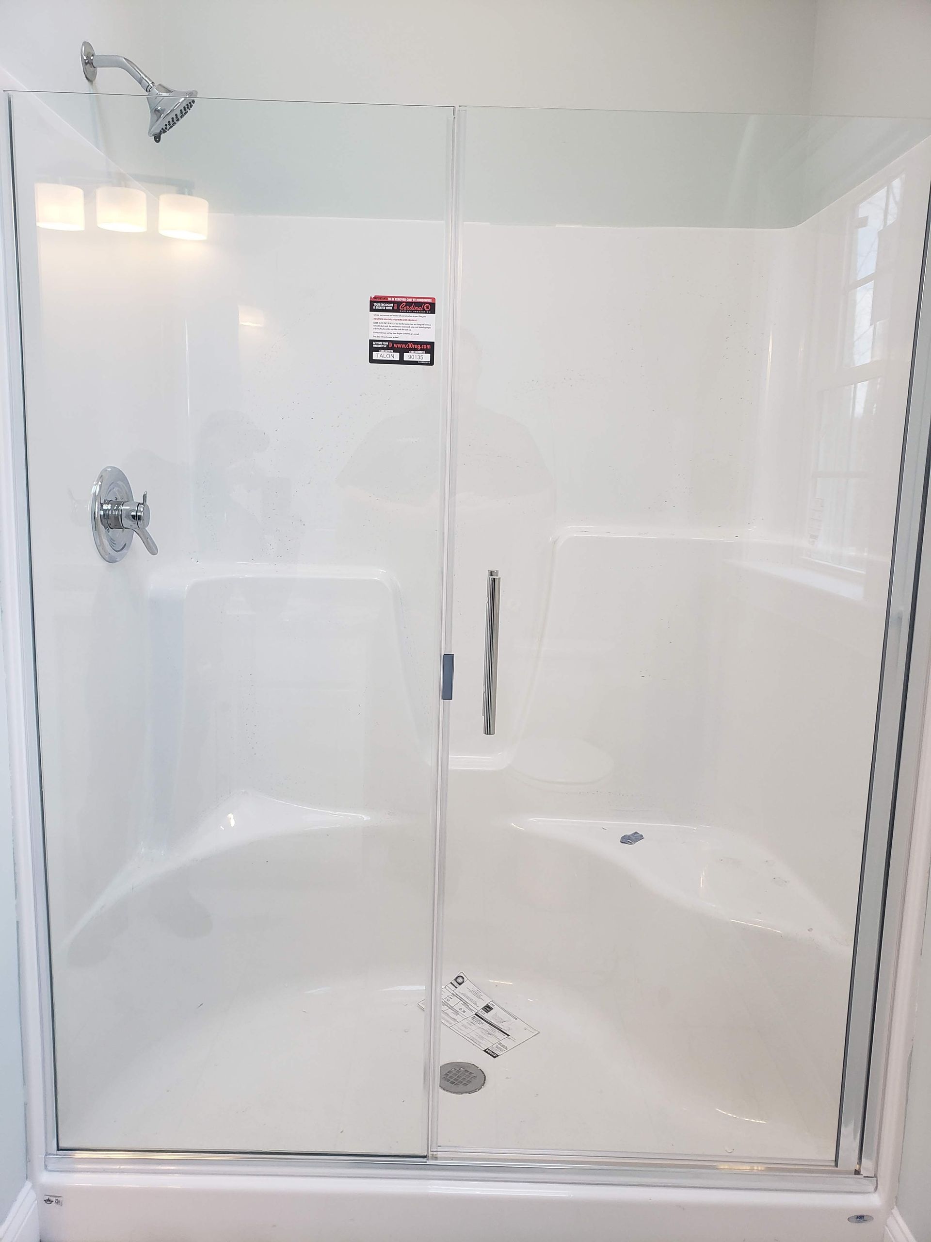 White shower stall with sliding glass doors, chrome fixtures, and a low curb.
