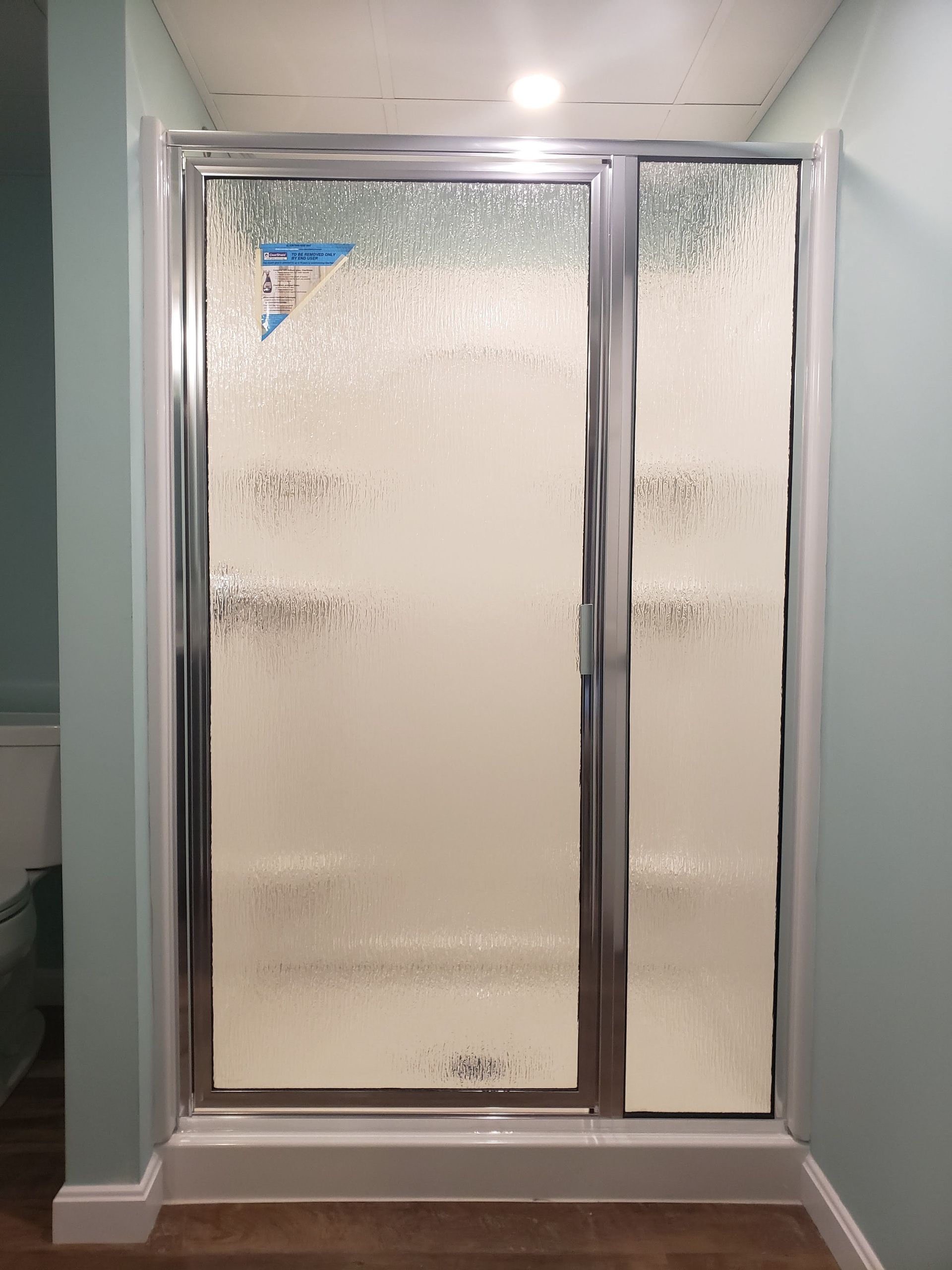 Shower with frosted glass doors and chrome frame against pale blue walls.